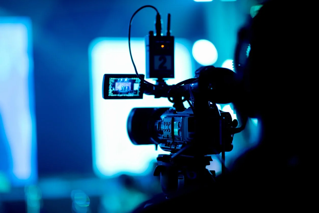 Professional video camera filming on a tripod in a blue-lit studio