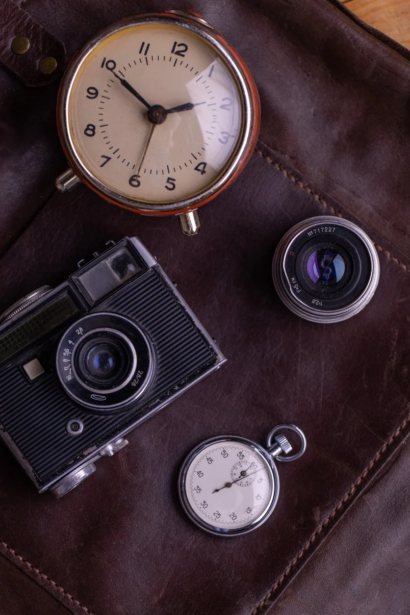 Vintage camera, clock, camera lens, and stopwatch arranged on a brown leather case