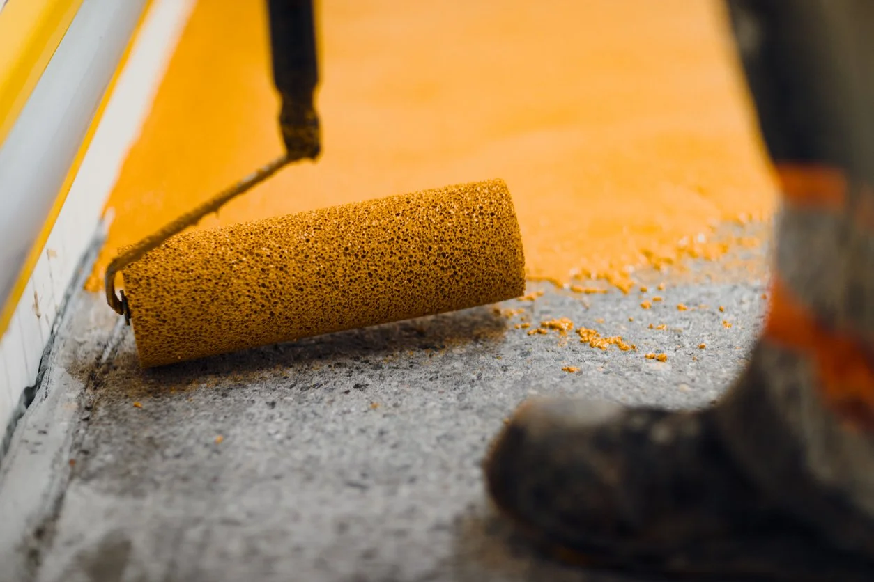 Paint roller applying orange paint to a concrete floor