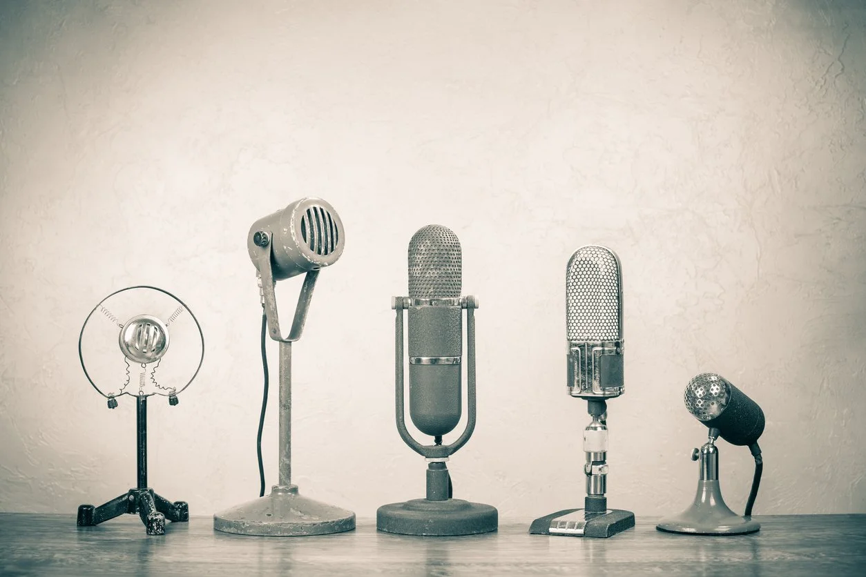 Five vintage microphones displayed on a tabletop against a textured wall