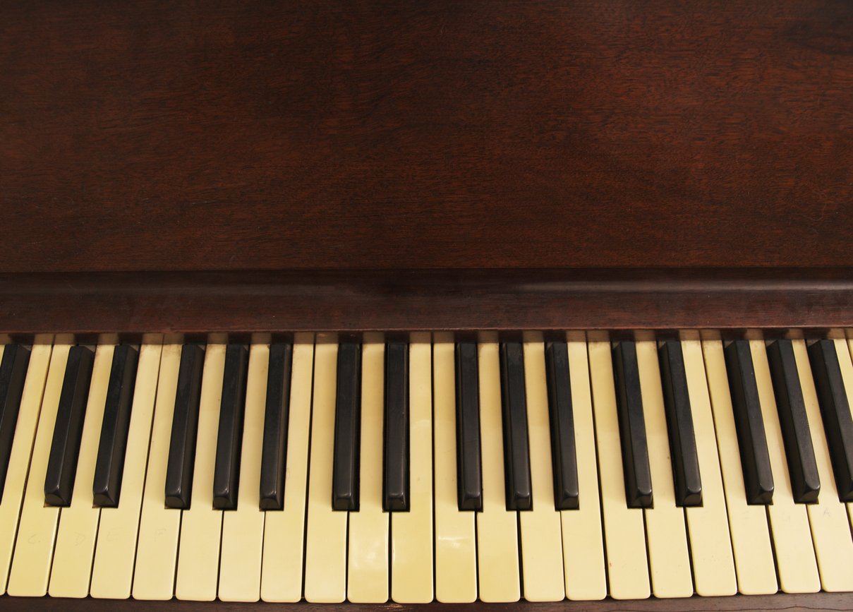 Close-up of vintage piano keys beneath a dark wooden panel