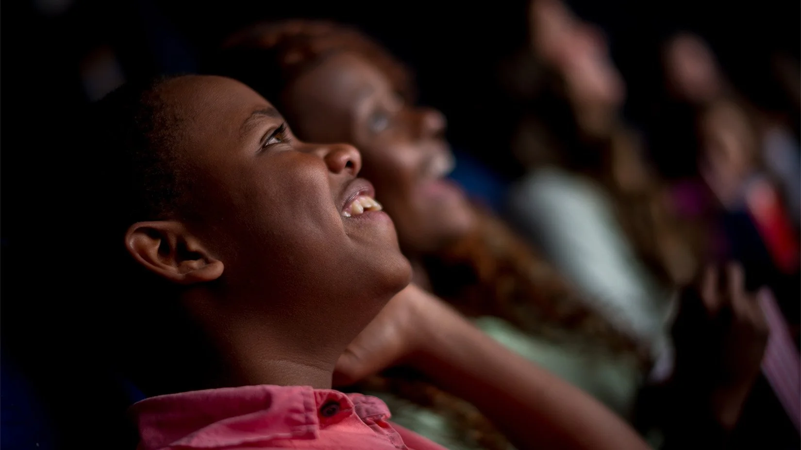 Smiling Black child watching a live theatrical event with other children in the background