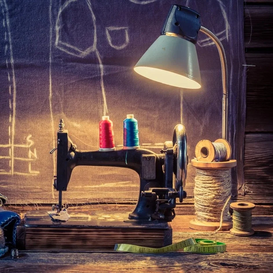 Vintage black sewing machine with colorful thread spools, measuring tape, and desk lamp on a rustic wooden table