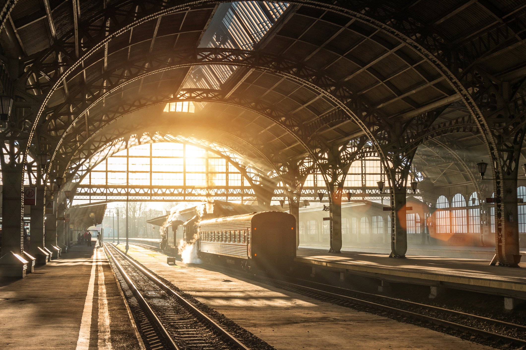 Steam locomotive and passenger train inside a historic railway station bathed in golden sunlight