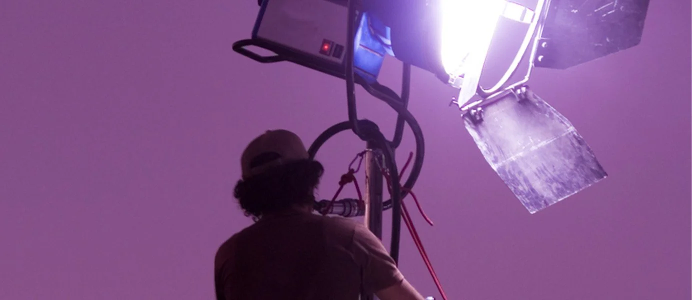 Film crew member operating a studio light and camera equipment in purple lighting