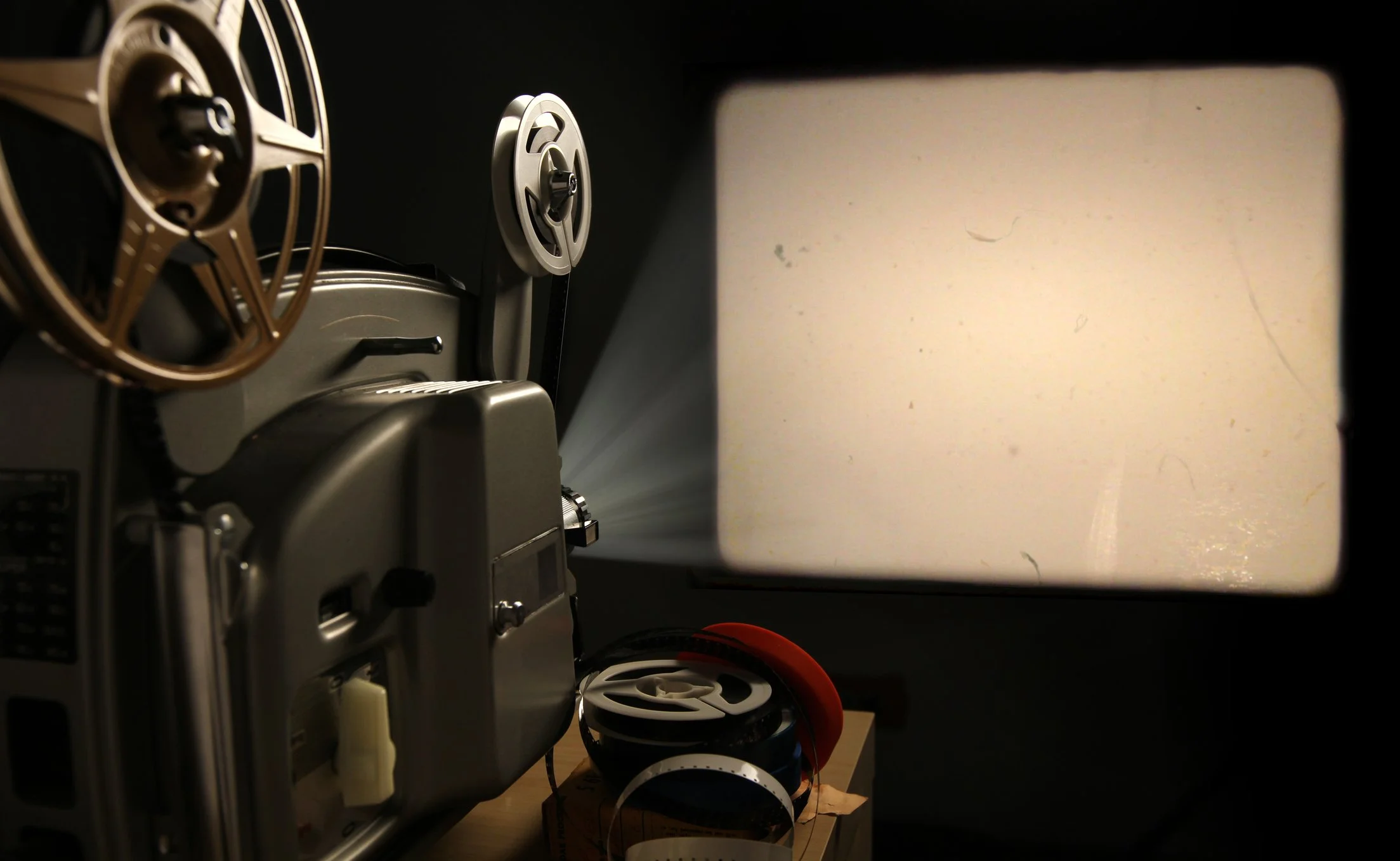 Vintage film projector with reels beside a blank illuminated projection screen