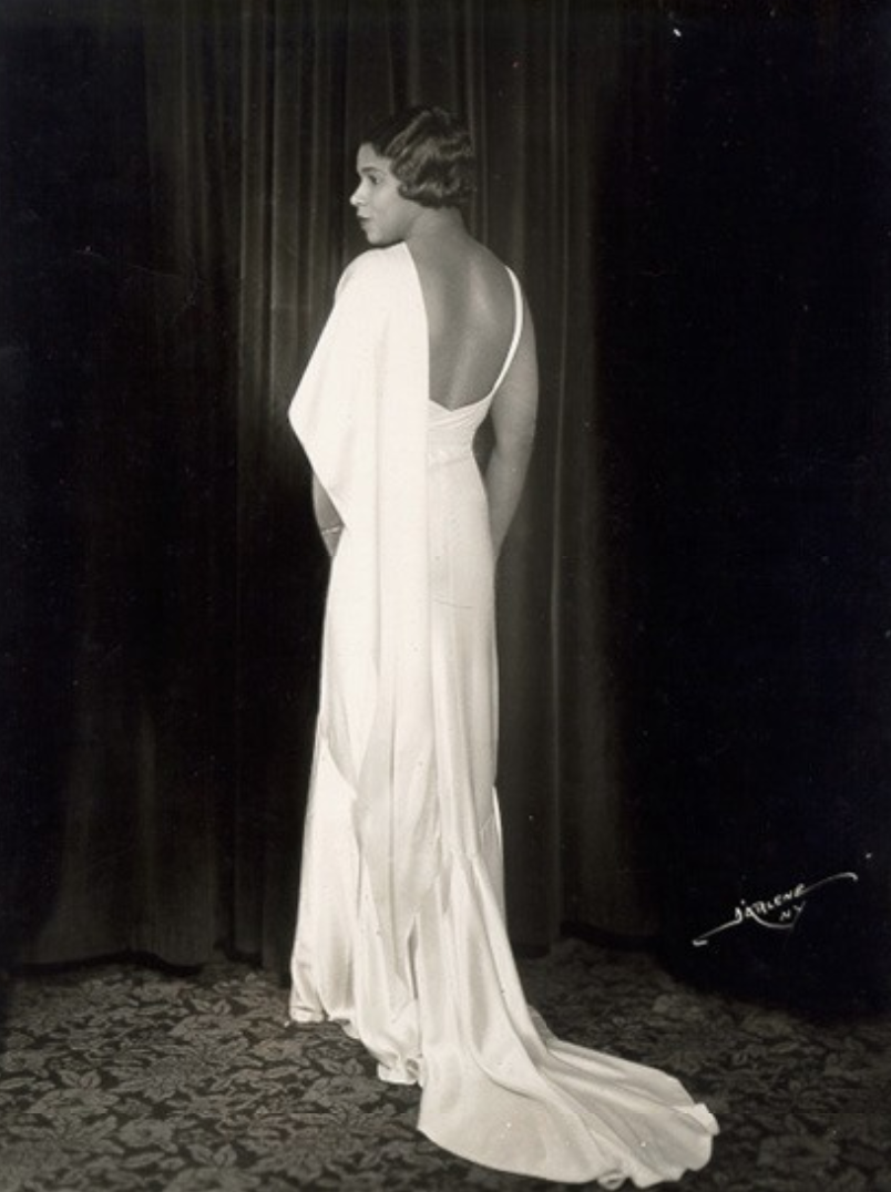 Vintage black-and-white photograph of Marian Anderson modeling a long white, backless evening gown with a train.