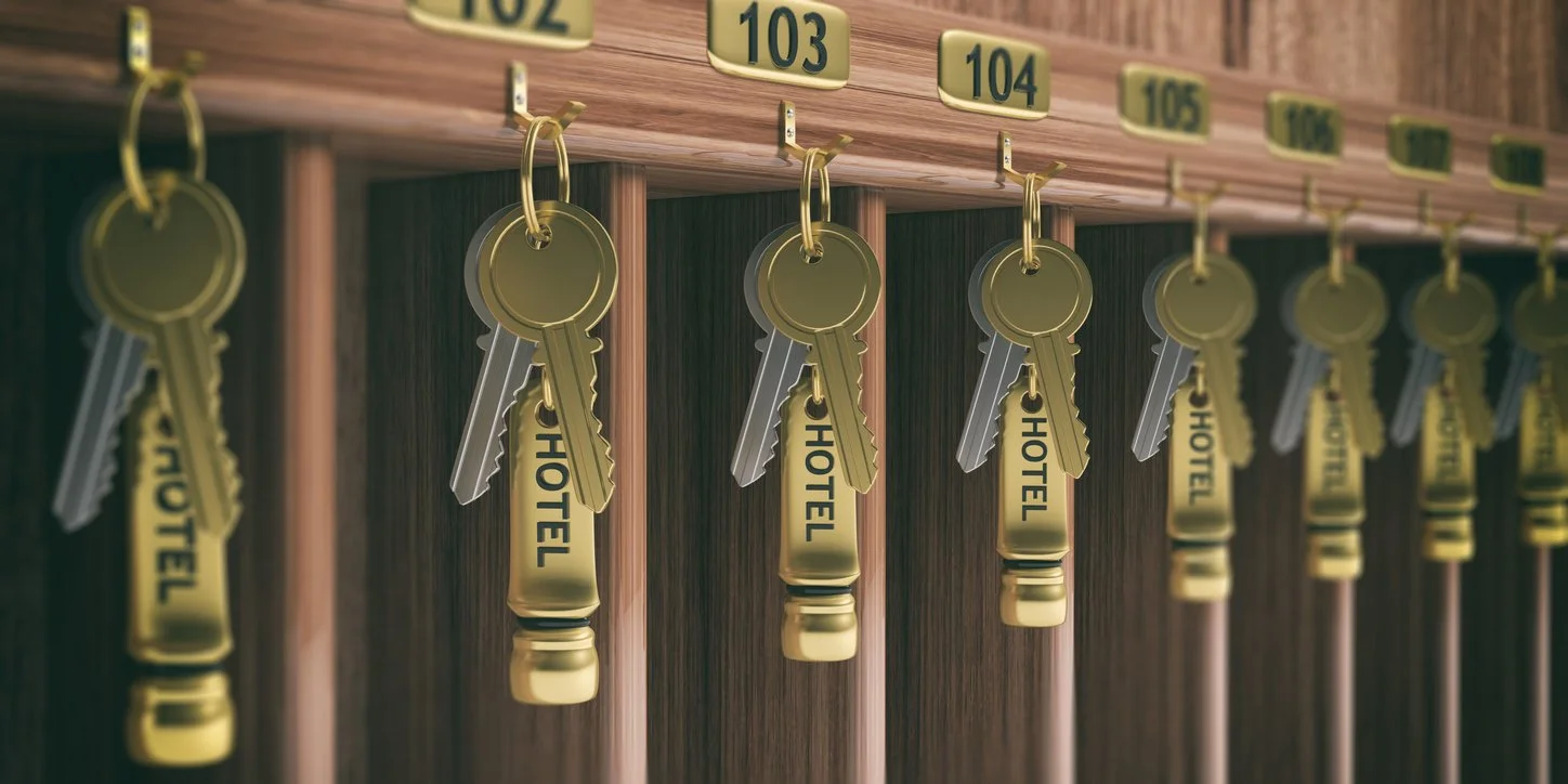 Hotel room keys labeled 102 through 107 hanging on wooden key hooks