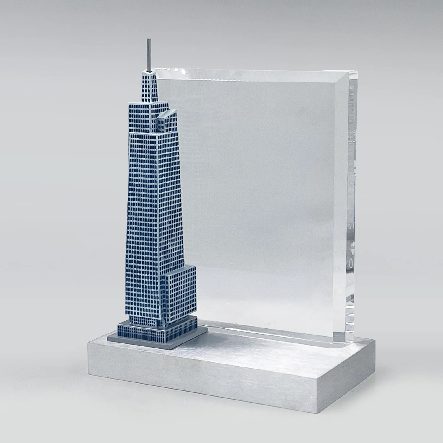 Real estate deal toy with a detailed skyscraper model beside a clear upright panel on a silver-colored base.