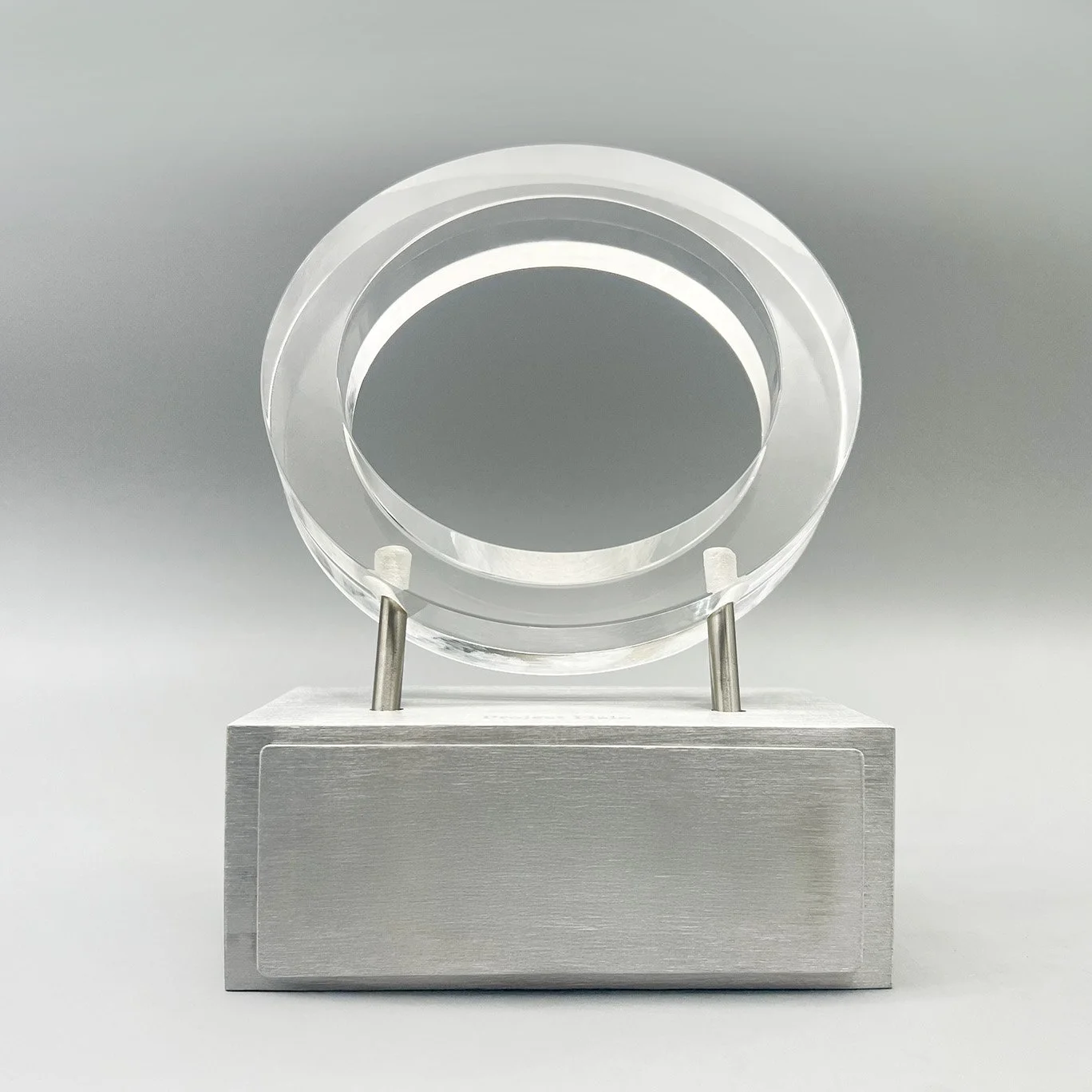 Circular clear Lucite corporate award supported by metal posts on a brushed-silver base.
