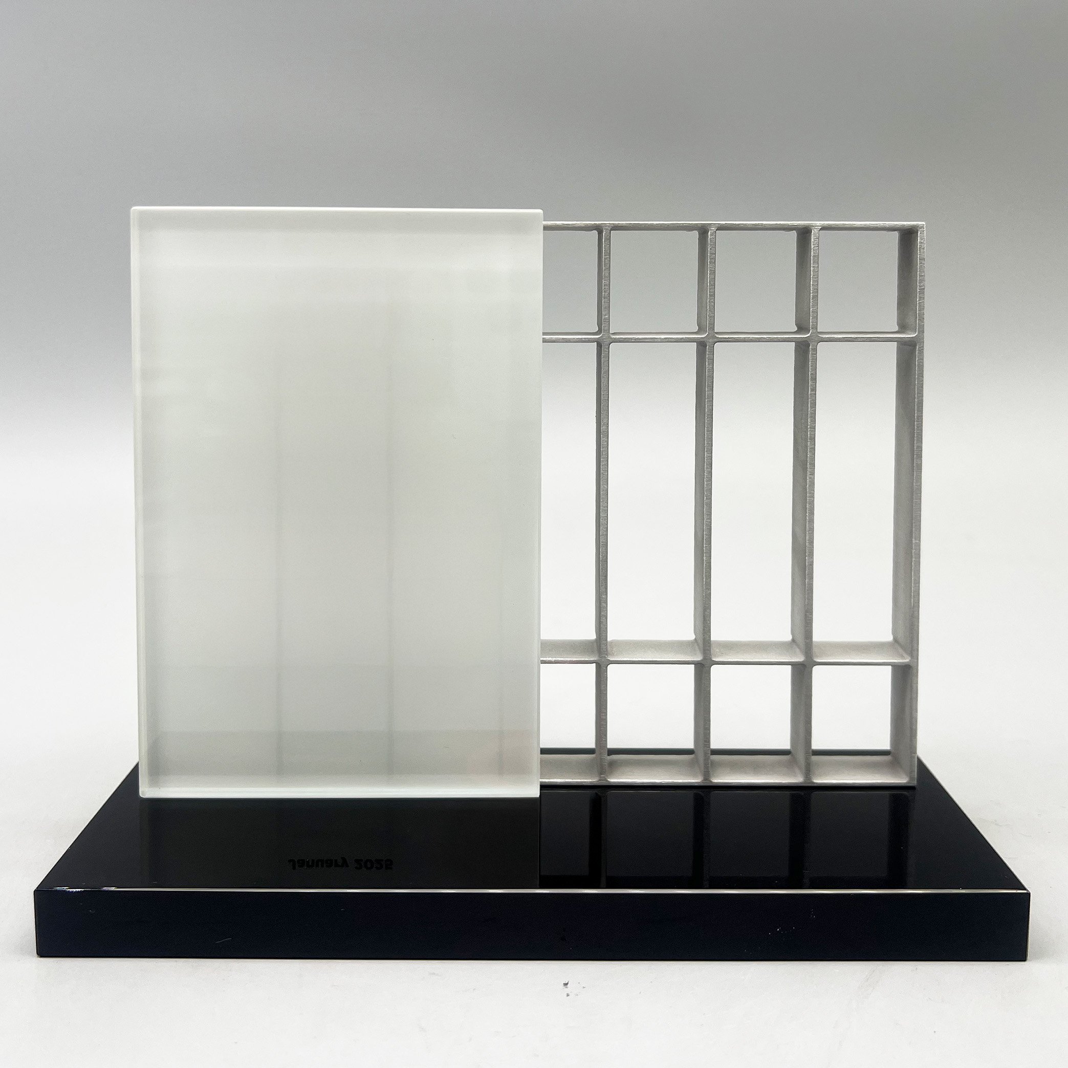 Custom architectural award combining a frosted Lucite panel and open metal grid on a glossy black base.