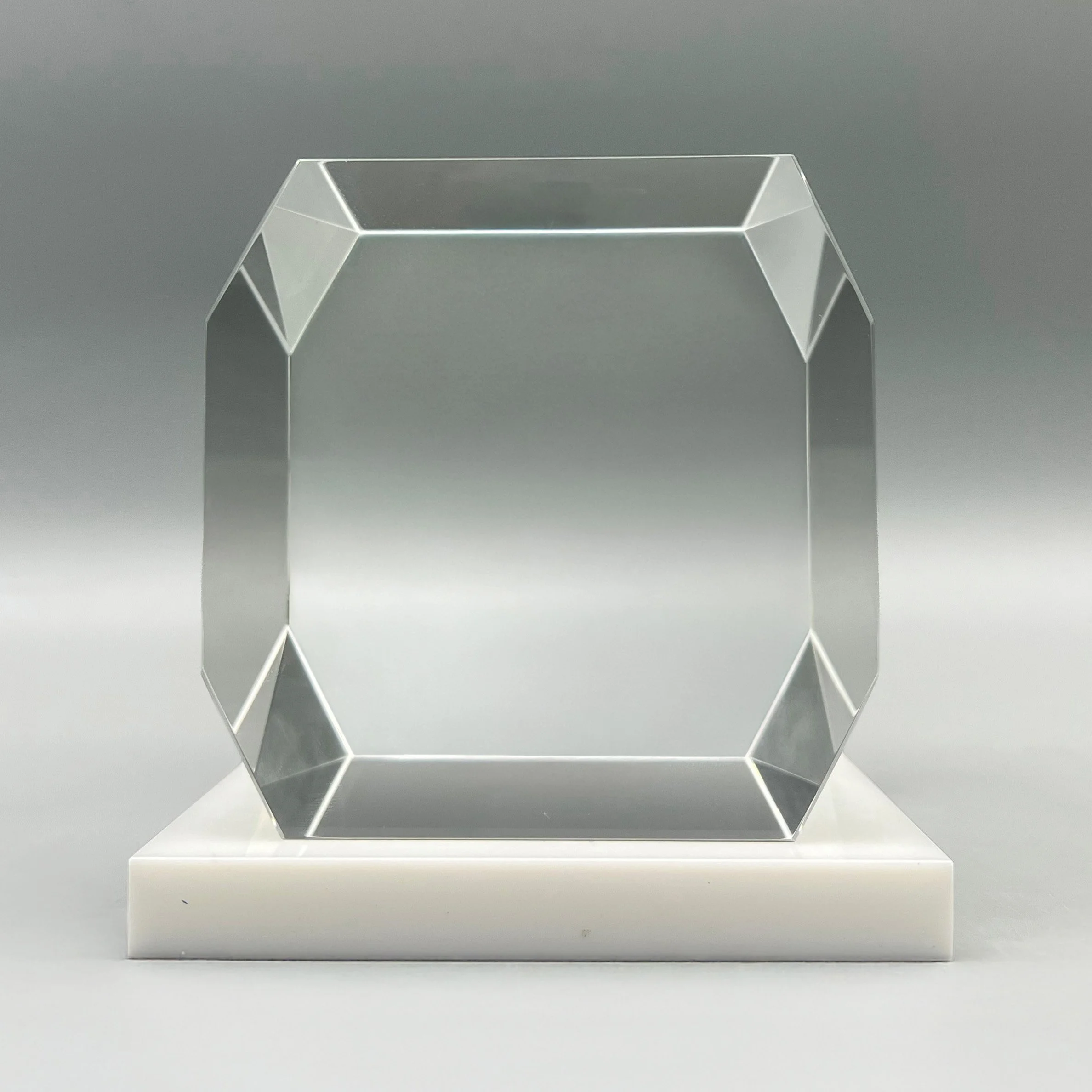 Clear faceted financial tombstone with polished beveled edges on a pale stone base.