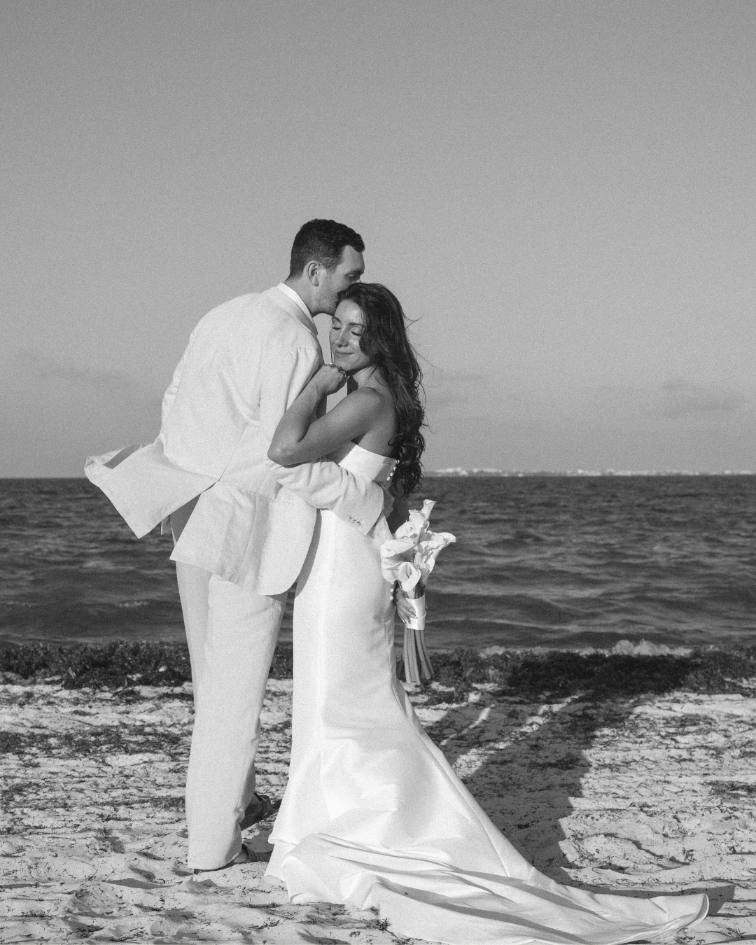 at the finest resort playa mujeres, this couple portrait at the beach is giving love by the way they hold eachother, the bouquet is in the back and the expression of the bride is serene by photographed in the sunset 