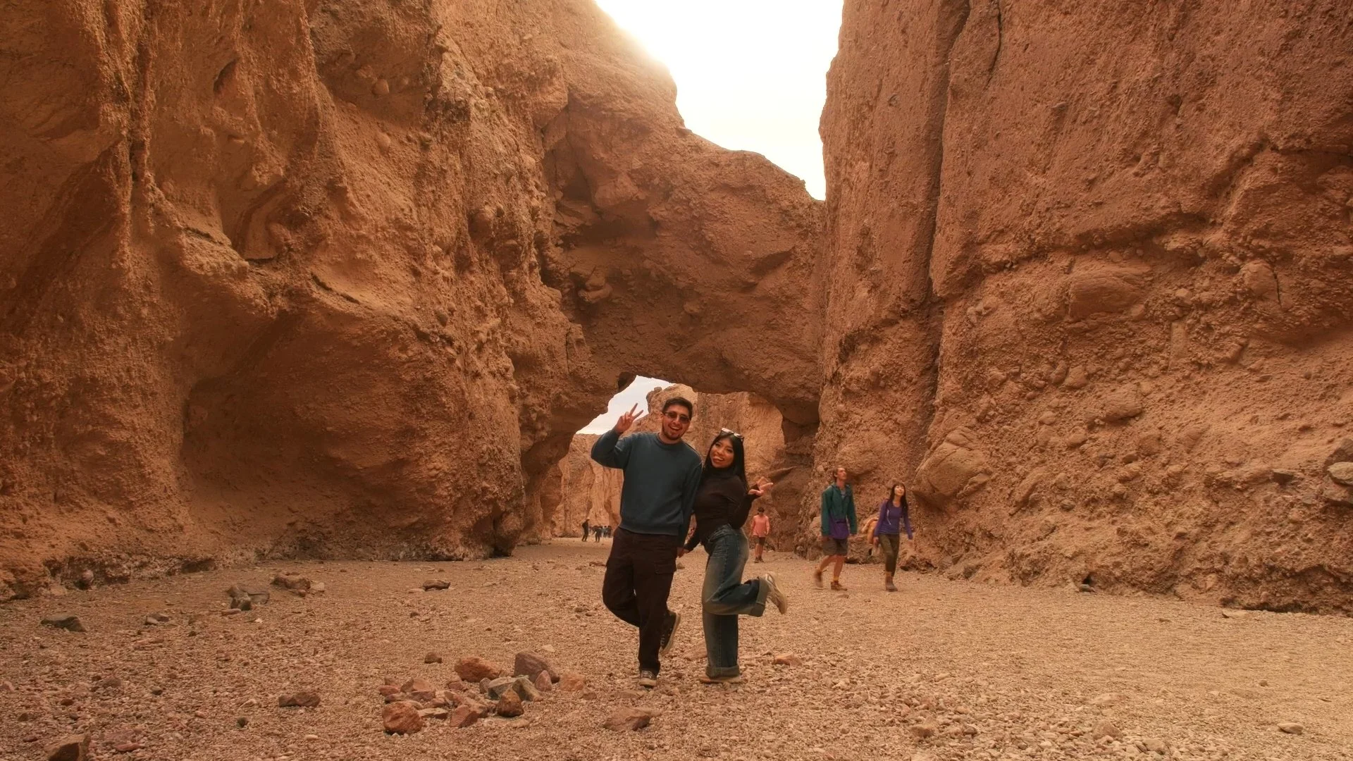People enjoying a hike through a narrow desert canyon with large reddish rock formations.
