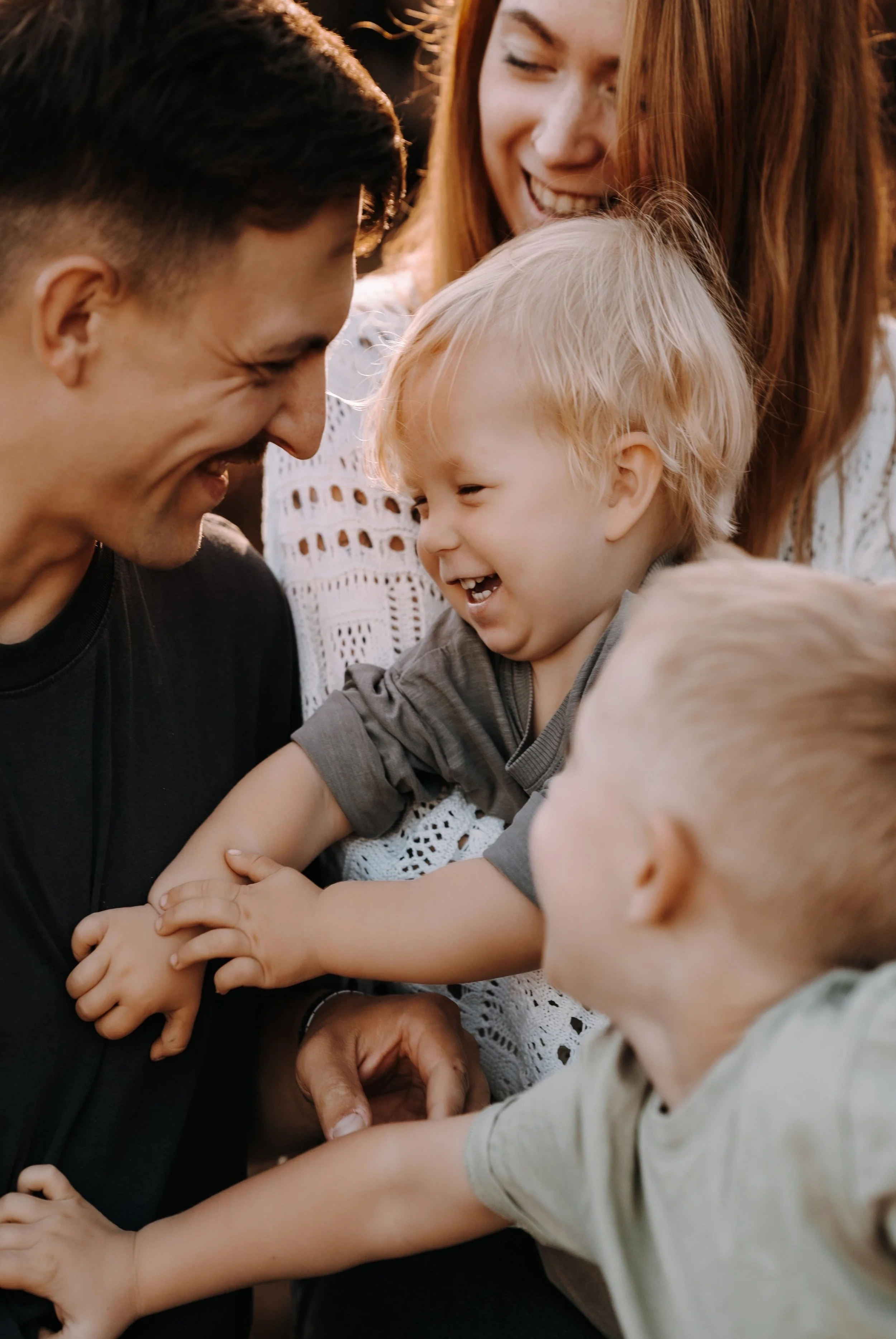 Eine lachende Familie, bestehend aus zwei Erwachsenen und drei Kindern, die sich gegenseitig umarmen und Arm in Arm sind, im Freien bei Sonnenuntergang.