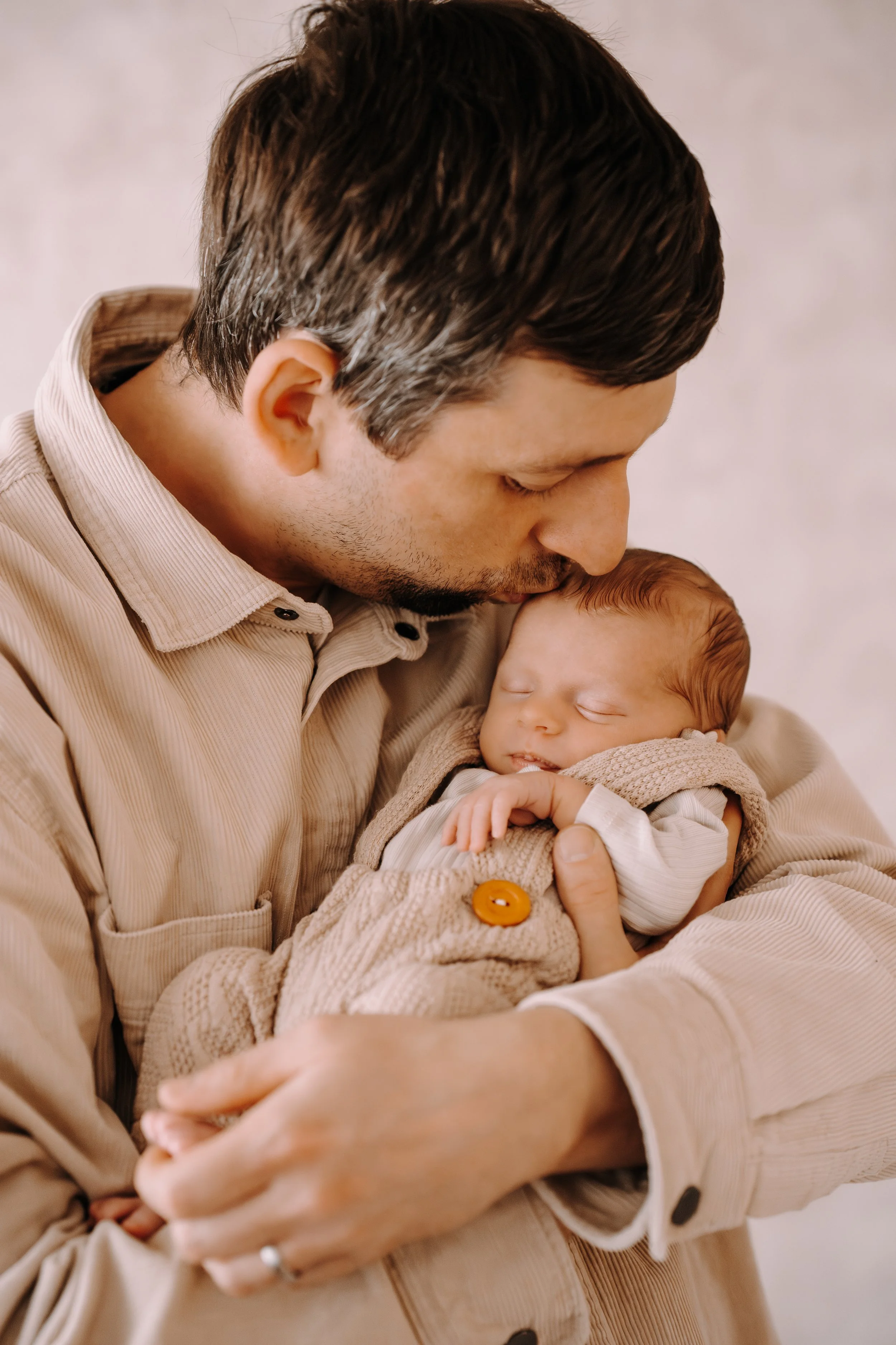 Vater hält schlafendes Baby in den Armen und küsst es auf die Stirn.