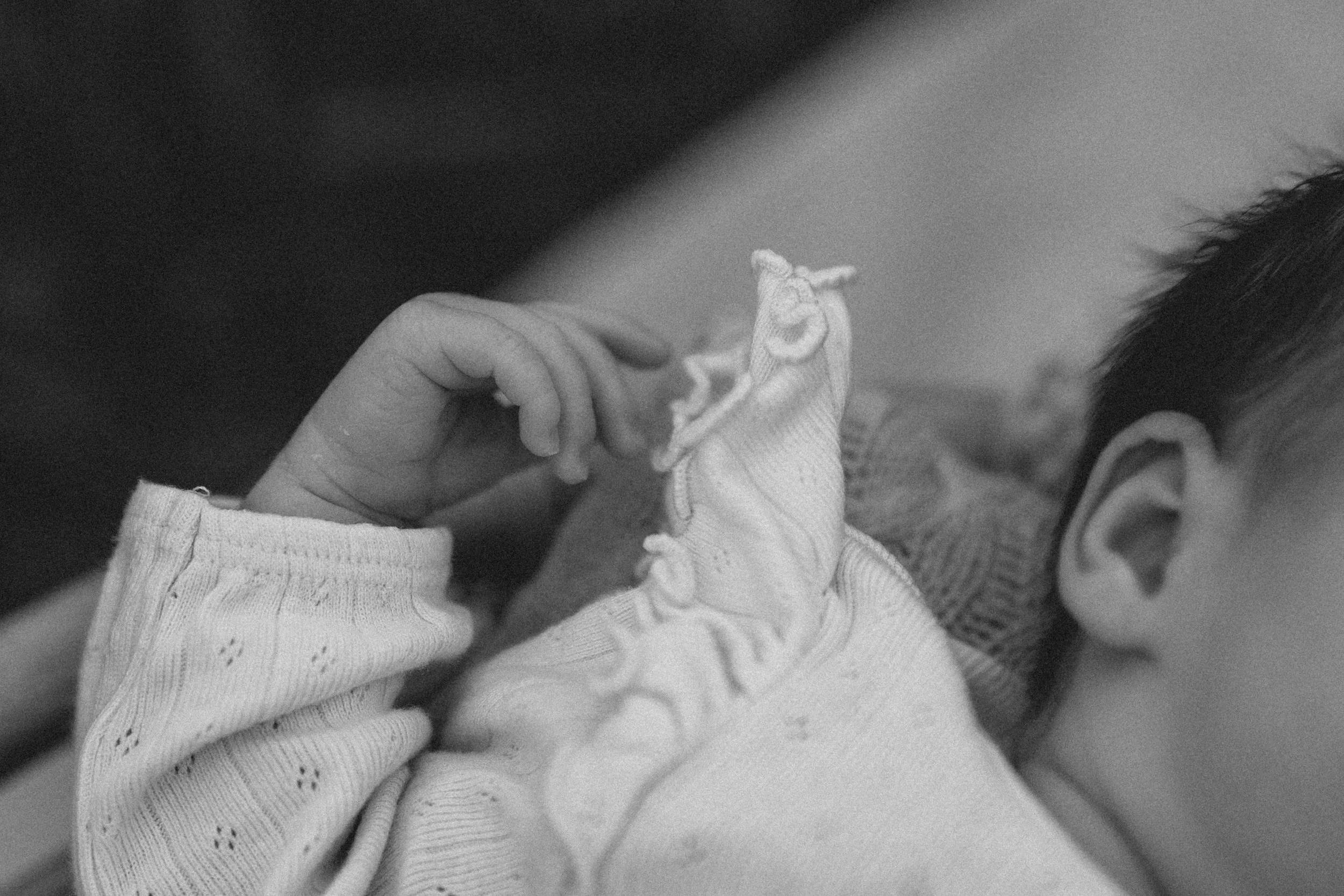 Nahaufnahme eines Kindes, das eine Hand eines Erwachsenen hält. Das Kind trägt ein gestricktes, langärmeliges Oberteil und eine kleine Stoffmütze.