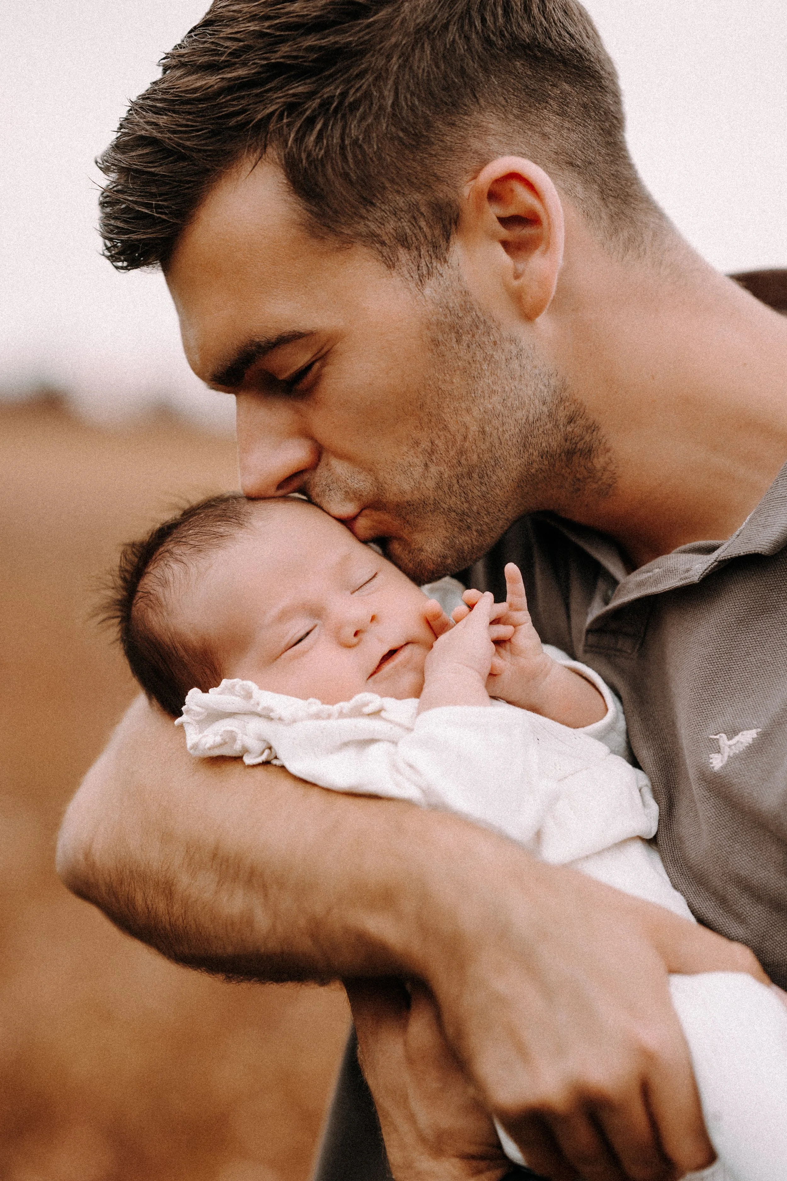 Ein Mann hält ein schlafendes Baby in den Armen und küsst es liebevoll auf die Stirn.