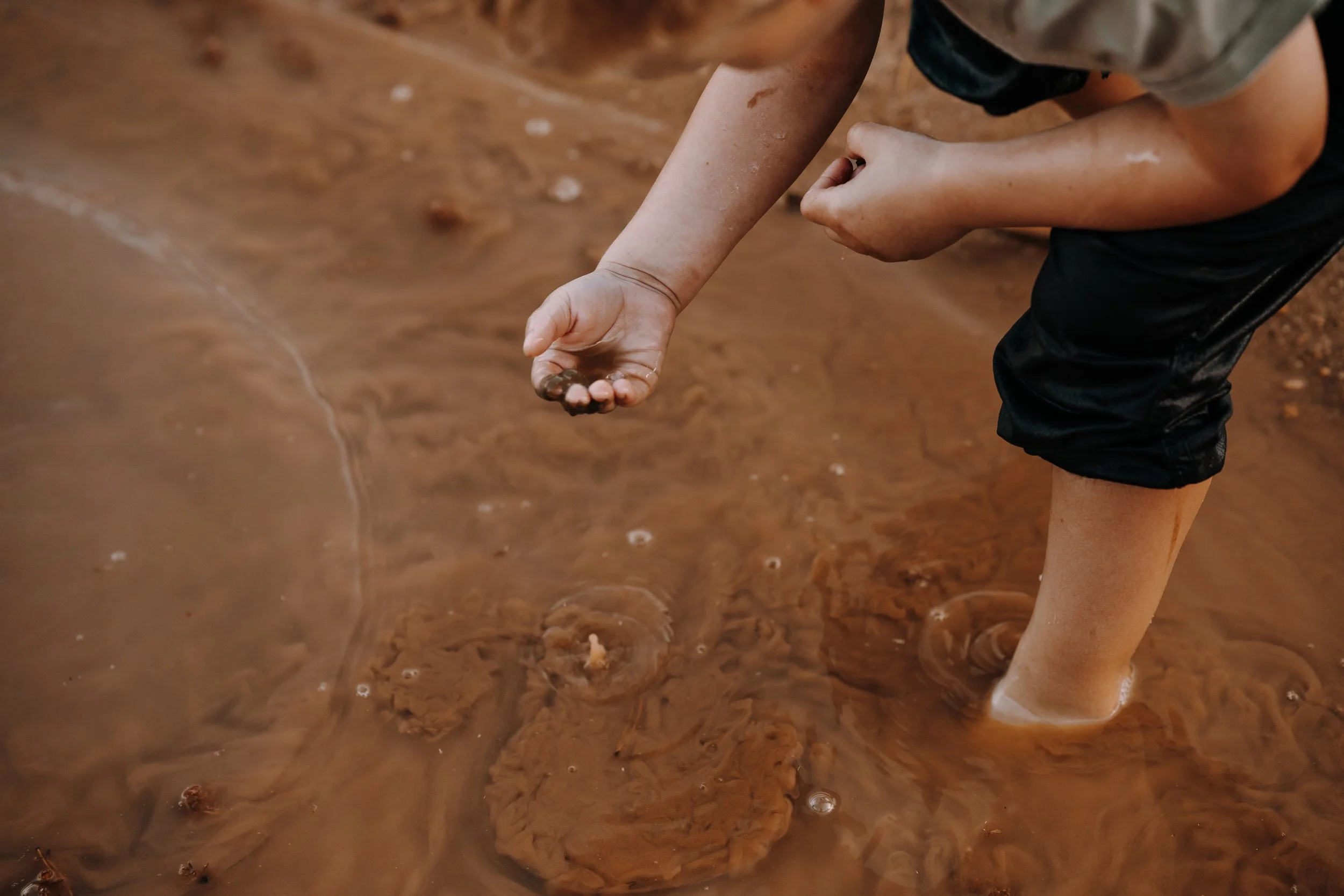 Ein Kind steht im Wasser und hält eine Stein in der Hand