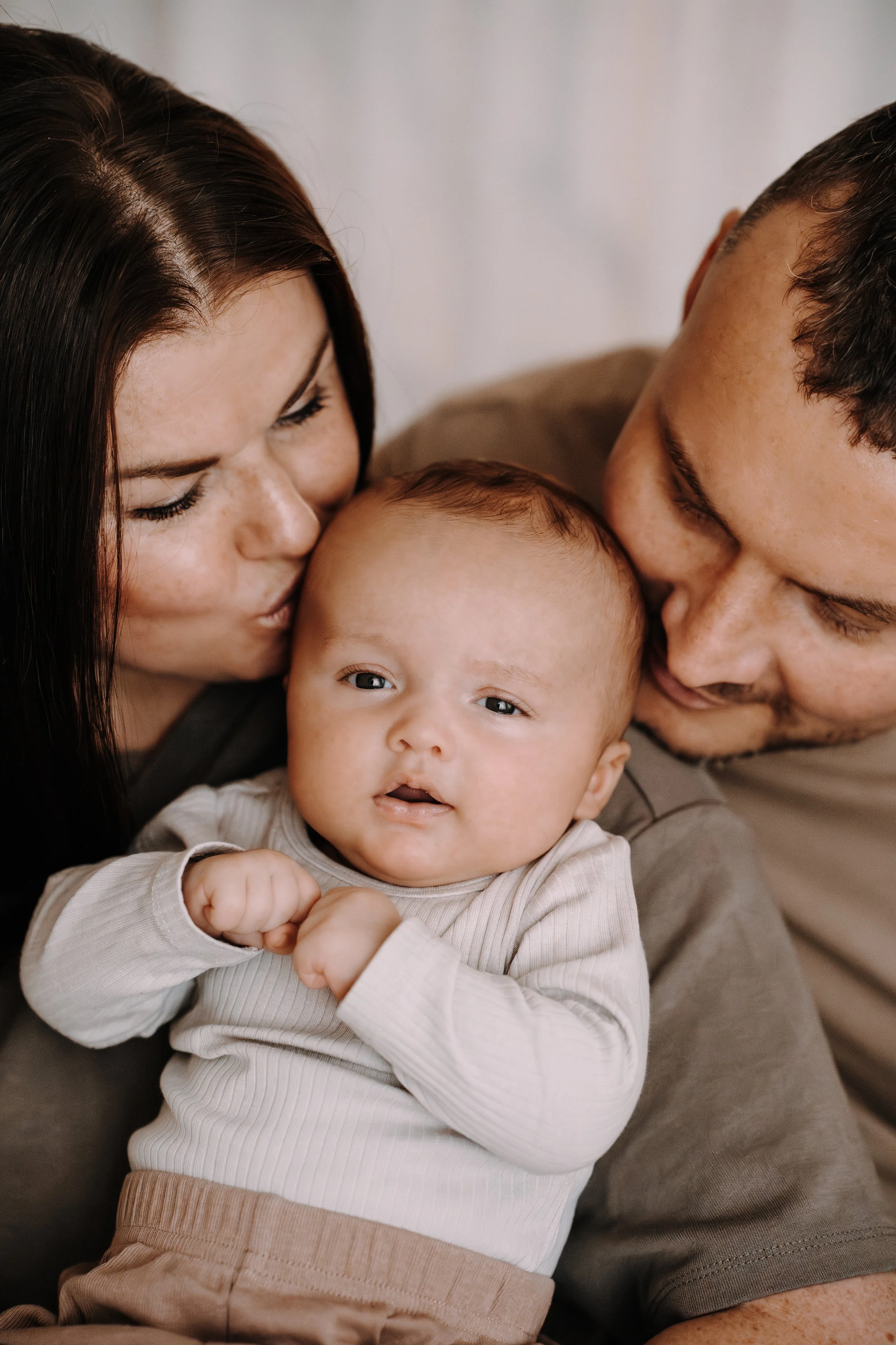 Ein Baby wird von einer Frau und einem Mann liebevoll umarmt und geküsst.