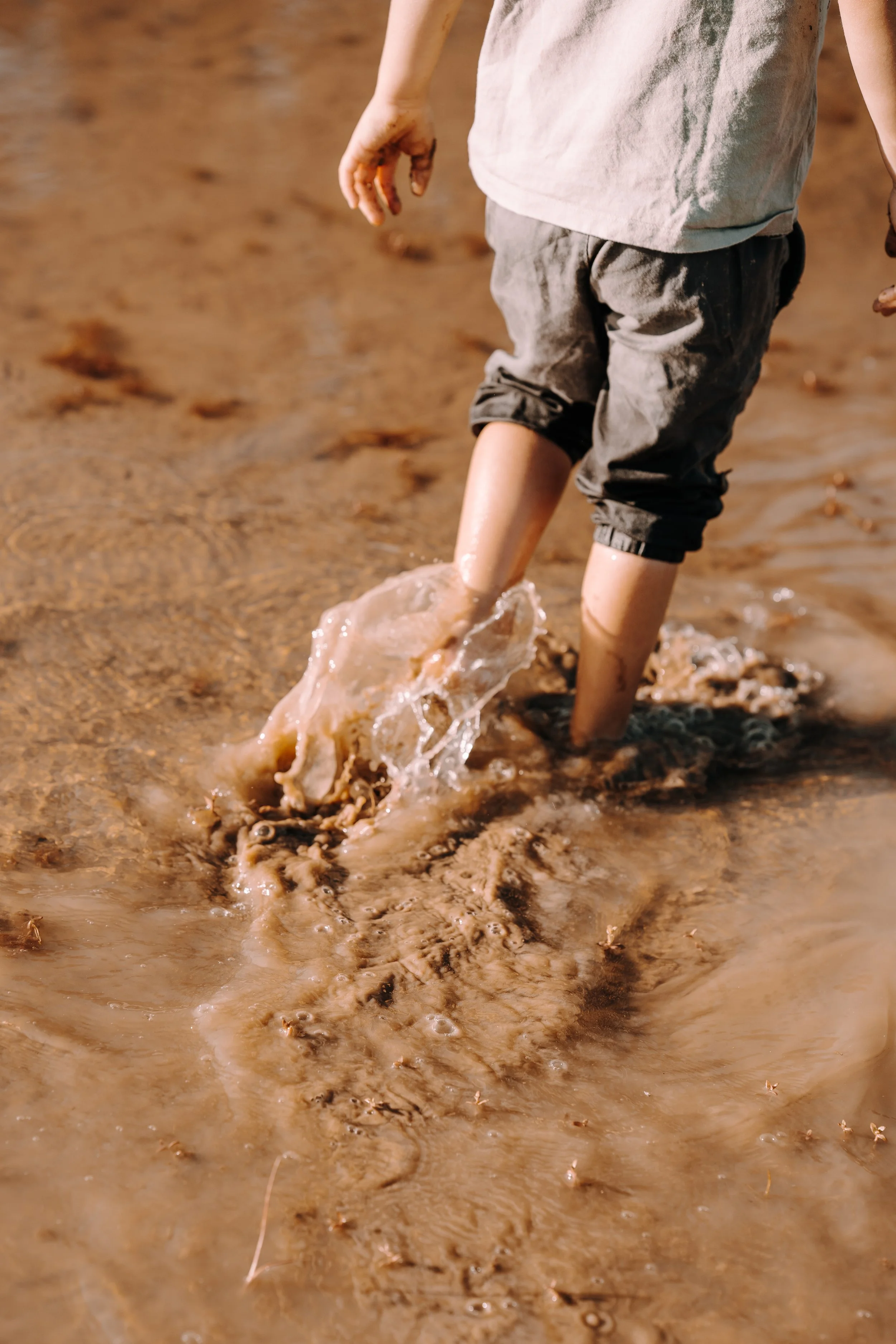 Ein Kind wackelt durch schlammiges Wasser mit nassen Shorts und schmutzigen Händen.