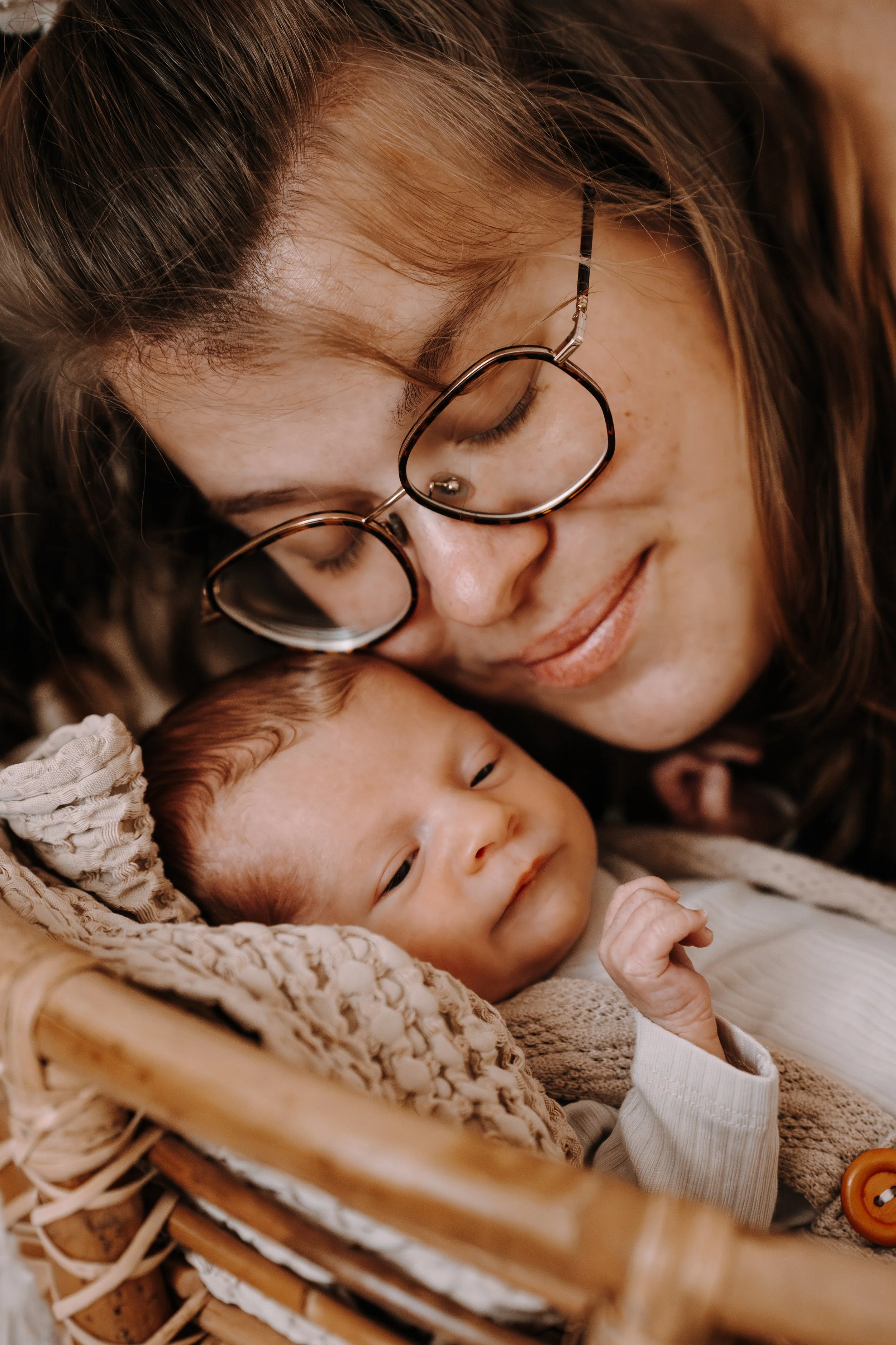Eine Frau mit Brille und braunen Haaren hält ein schlafendes Baby in einem Korb.