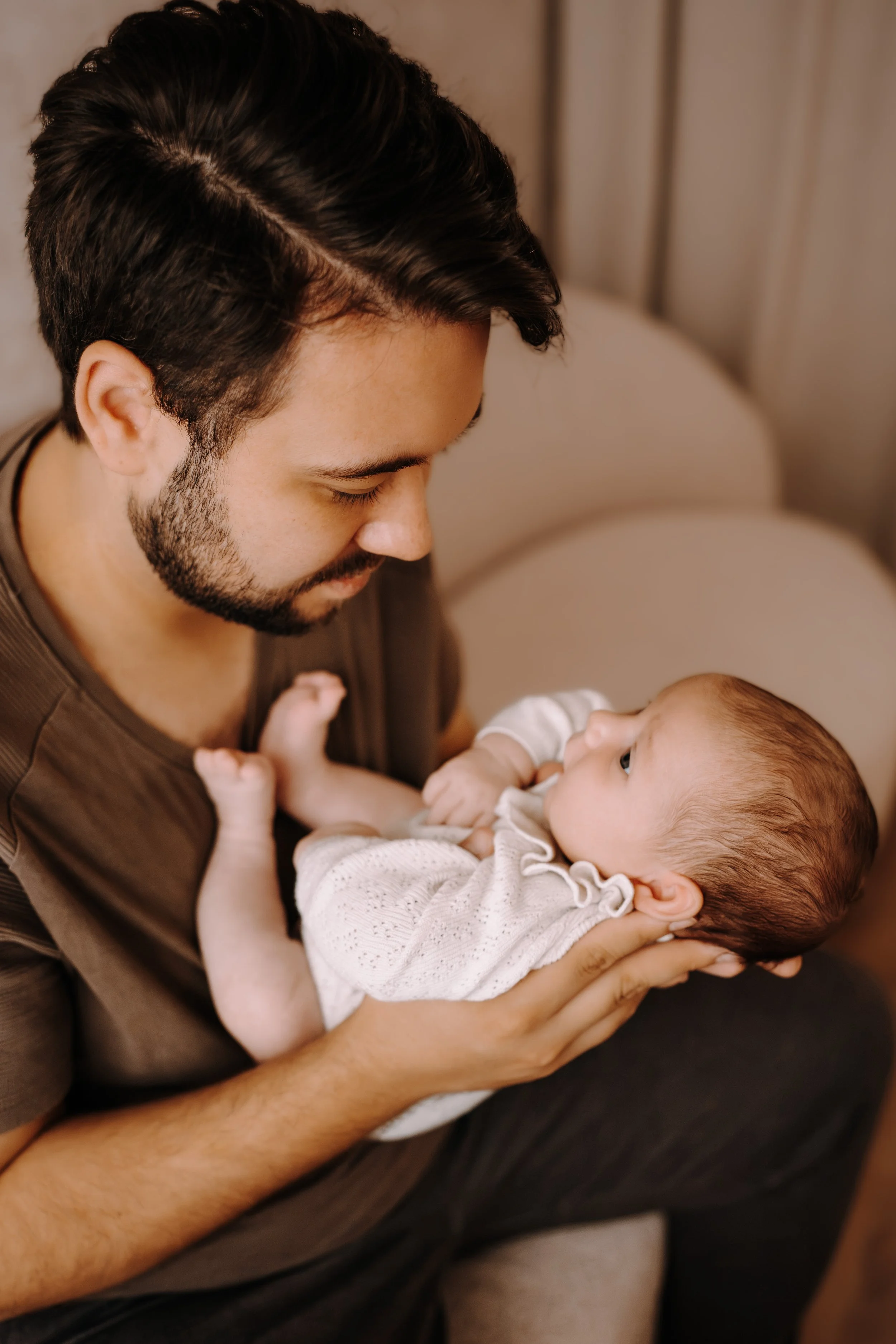 Ein Mann hält ein Baby in den Armen, Blickkontakt zwischen beiden, in einem warmen Raum.