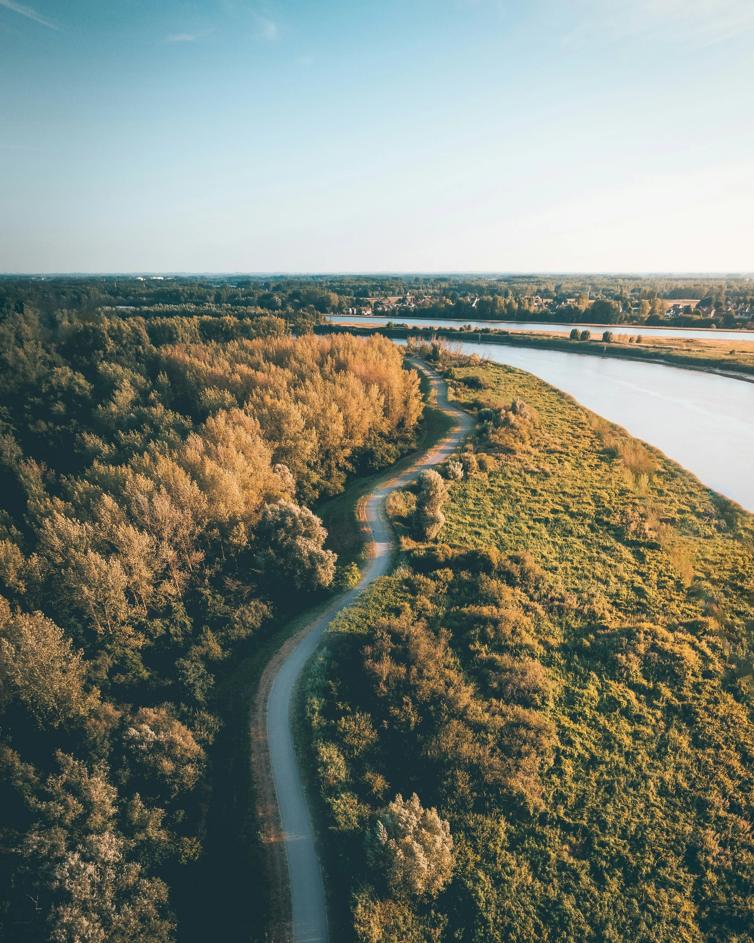 Een breed landschap met een kronkelende rivier, omringd door weelderige bomen en grasvelden, onder een heldere lucht.