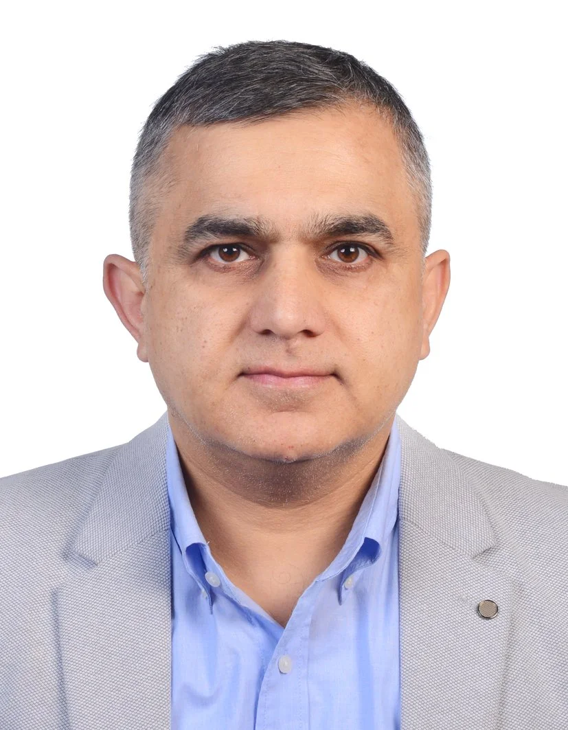 Portrait of a man in a light gray blazer and blue shirt against a white background.