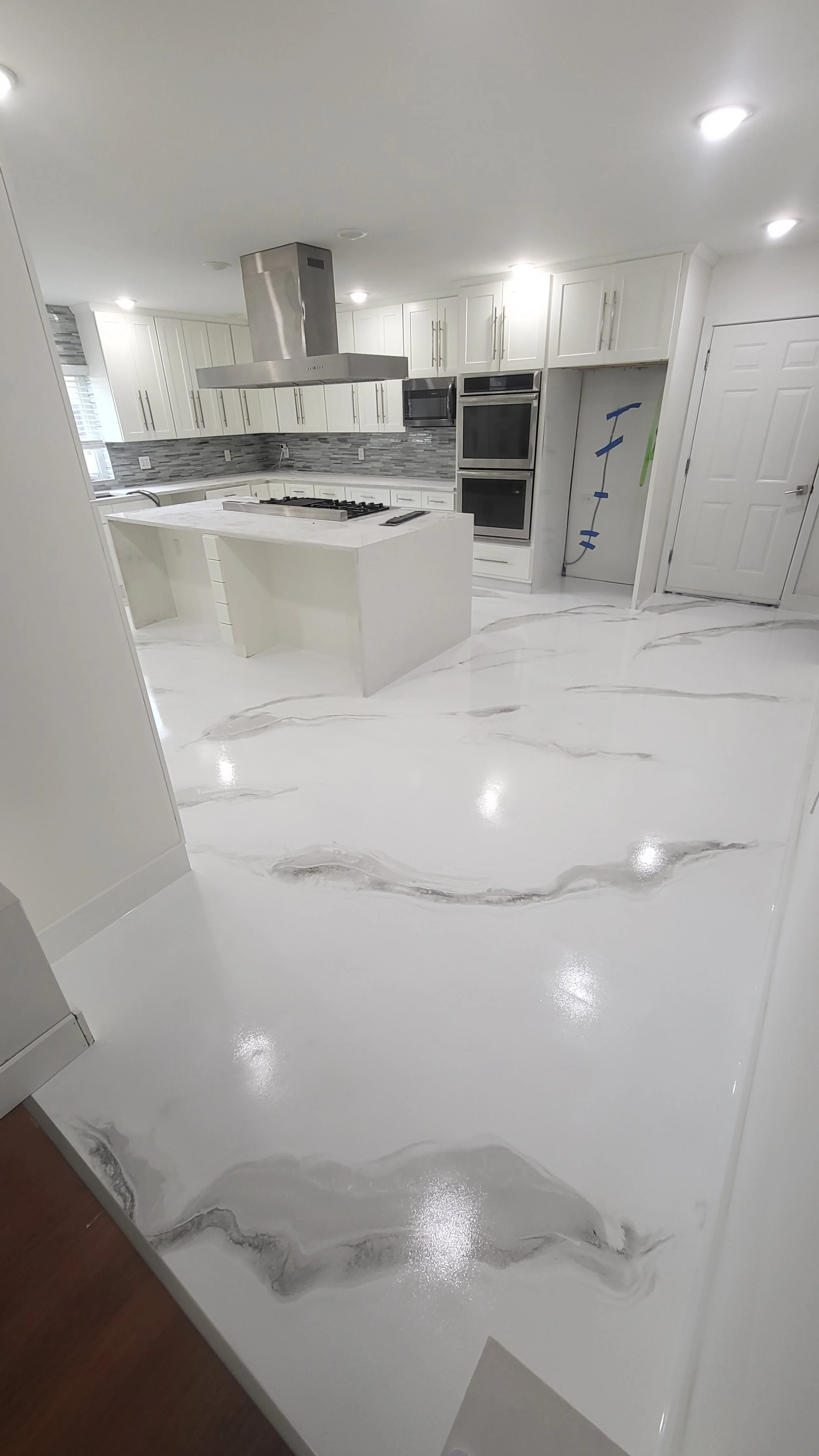 Modern kitchen with white cabinets, gray backsplash, white epoxy marble flooring, and a kitchen island with a gas stove and hanging stainless steel range hood.