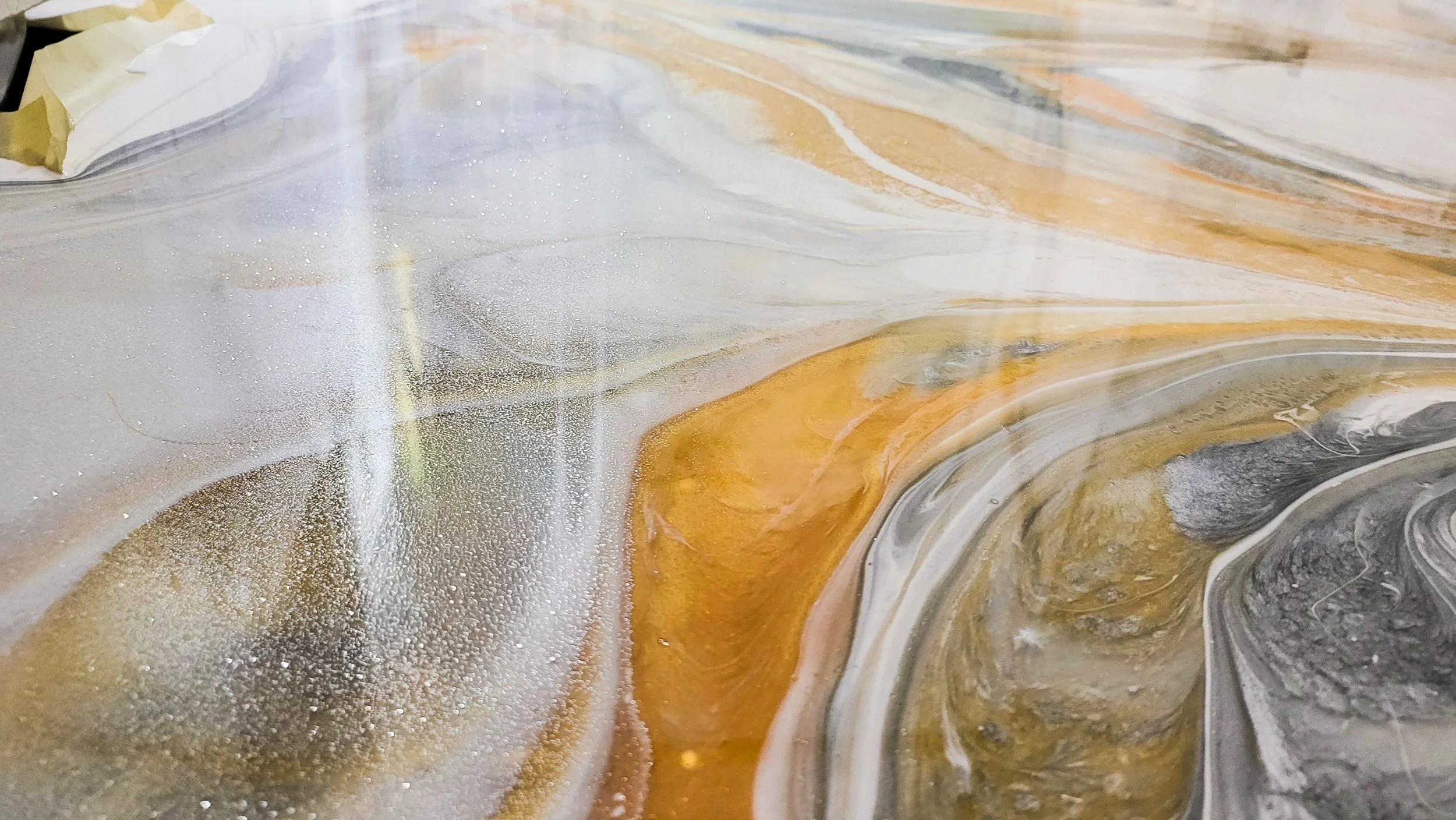 Close-up of an abstract epoxy marble surface with swirls of white, gray, black, and gold colors.