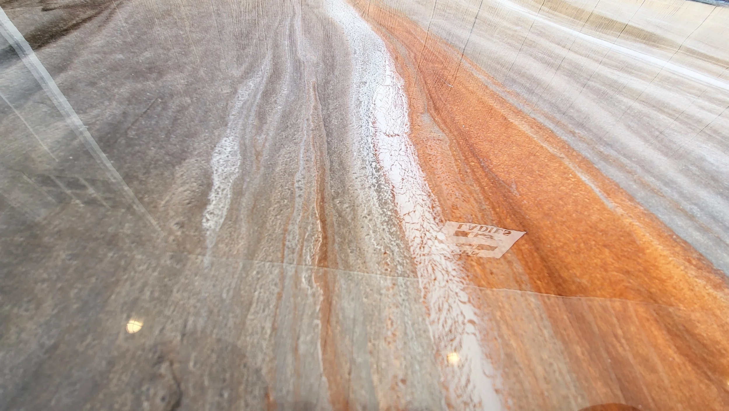 Close-up photograph of a polished epoxy marble floor with natural swirling patterns in shades of gray, white, and copper. The surface has a glossy finish that reflects light.