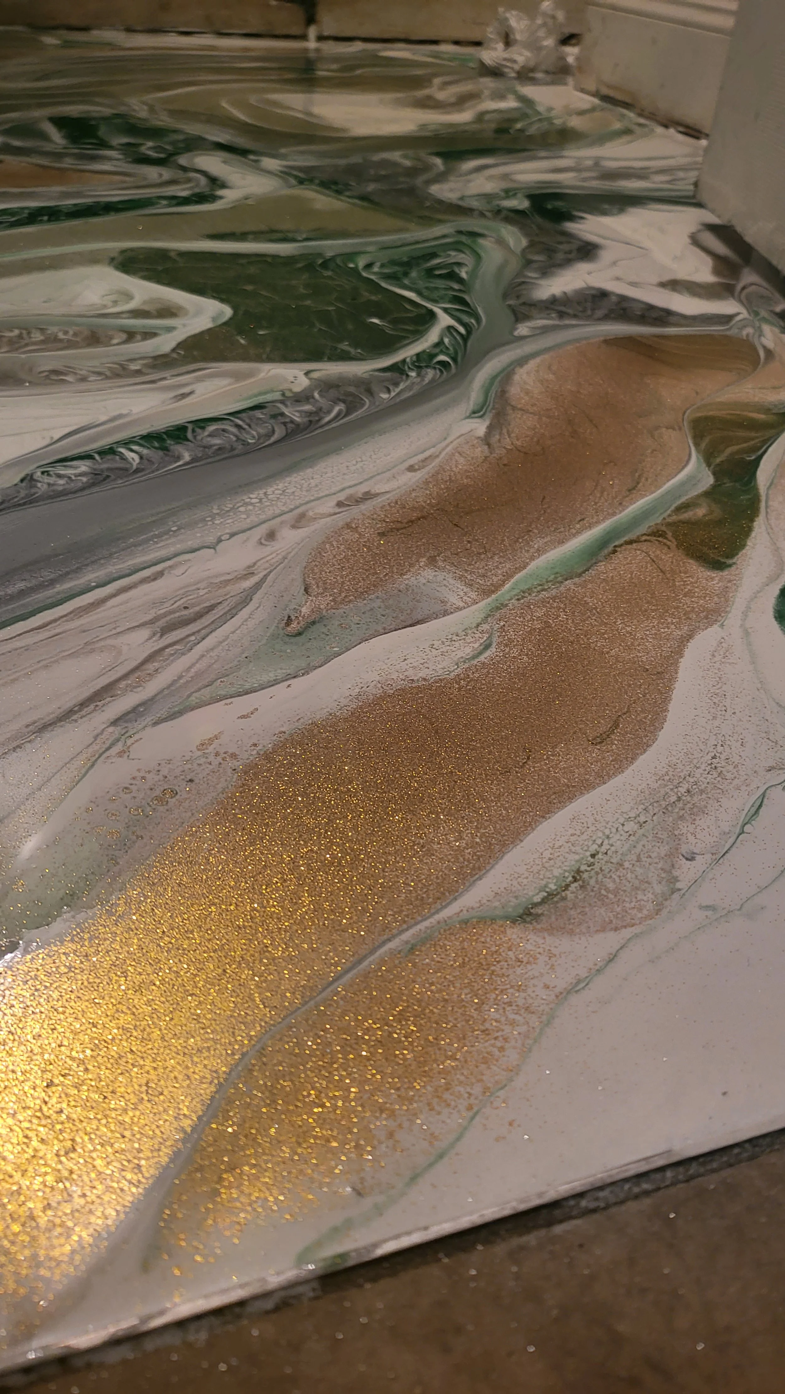 Abstract epoxy pour bathroom floor with swirling white, green, and gold textures.