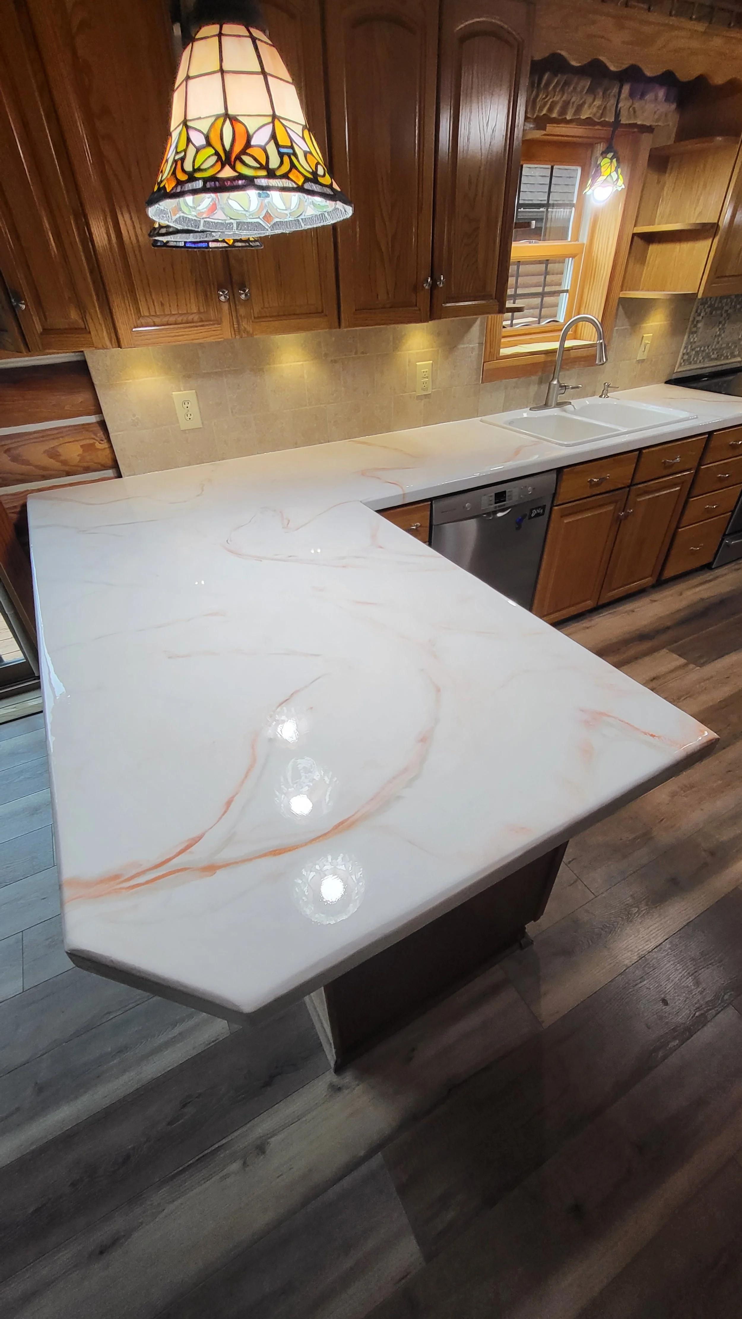 A kitchen with wooden cabinets, a marble epoxy countertop, a sink, and stained glass pendant lights.