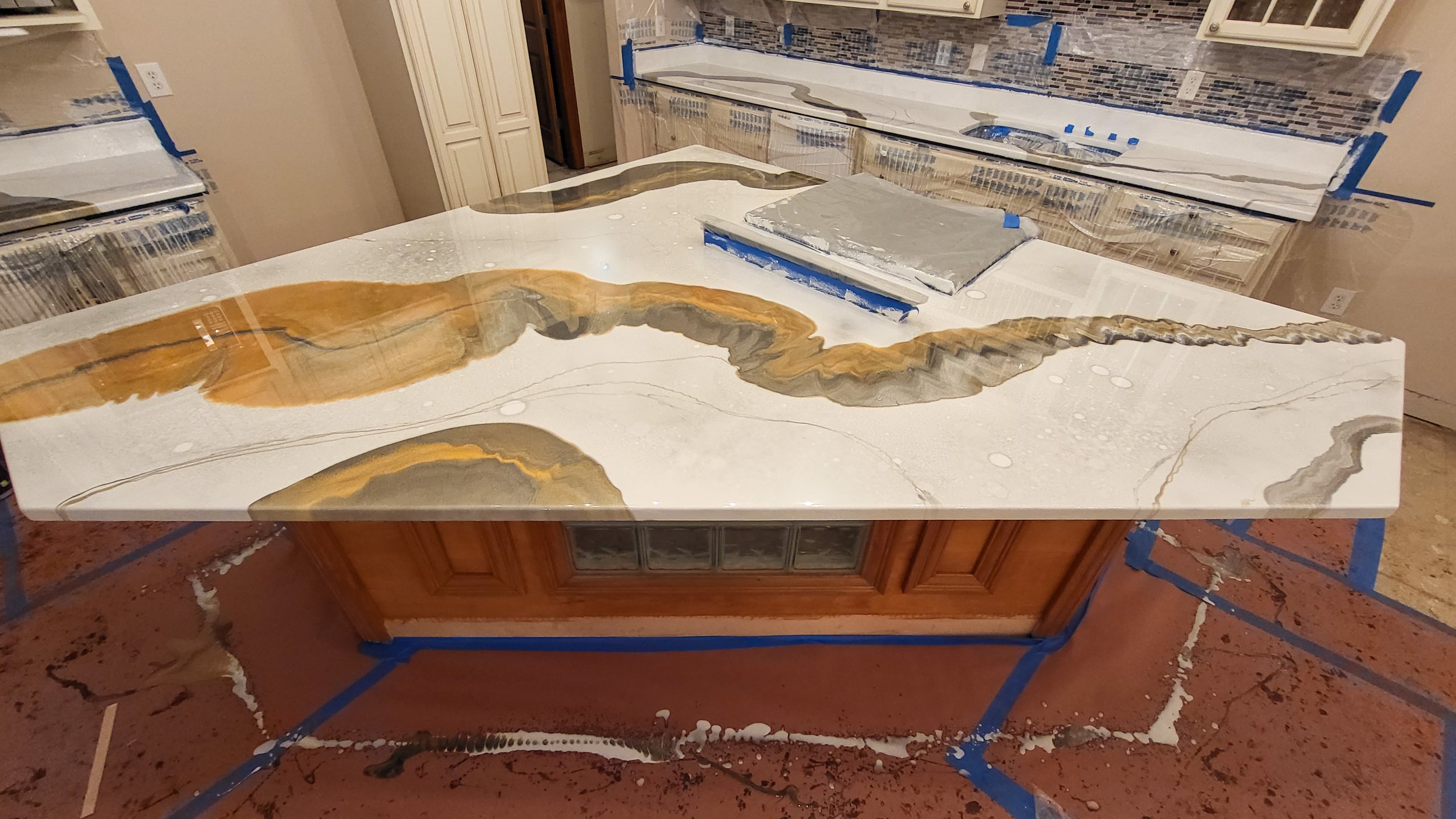 A kitchen island with a white and gold patterned marble epoxy countertop under construction, covered with painter's tape and protective sheet.