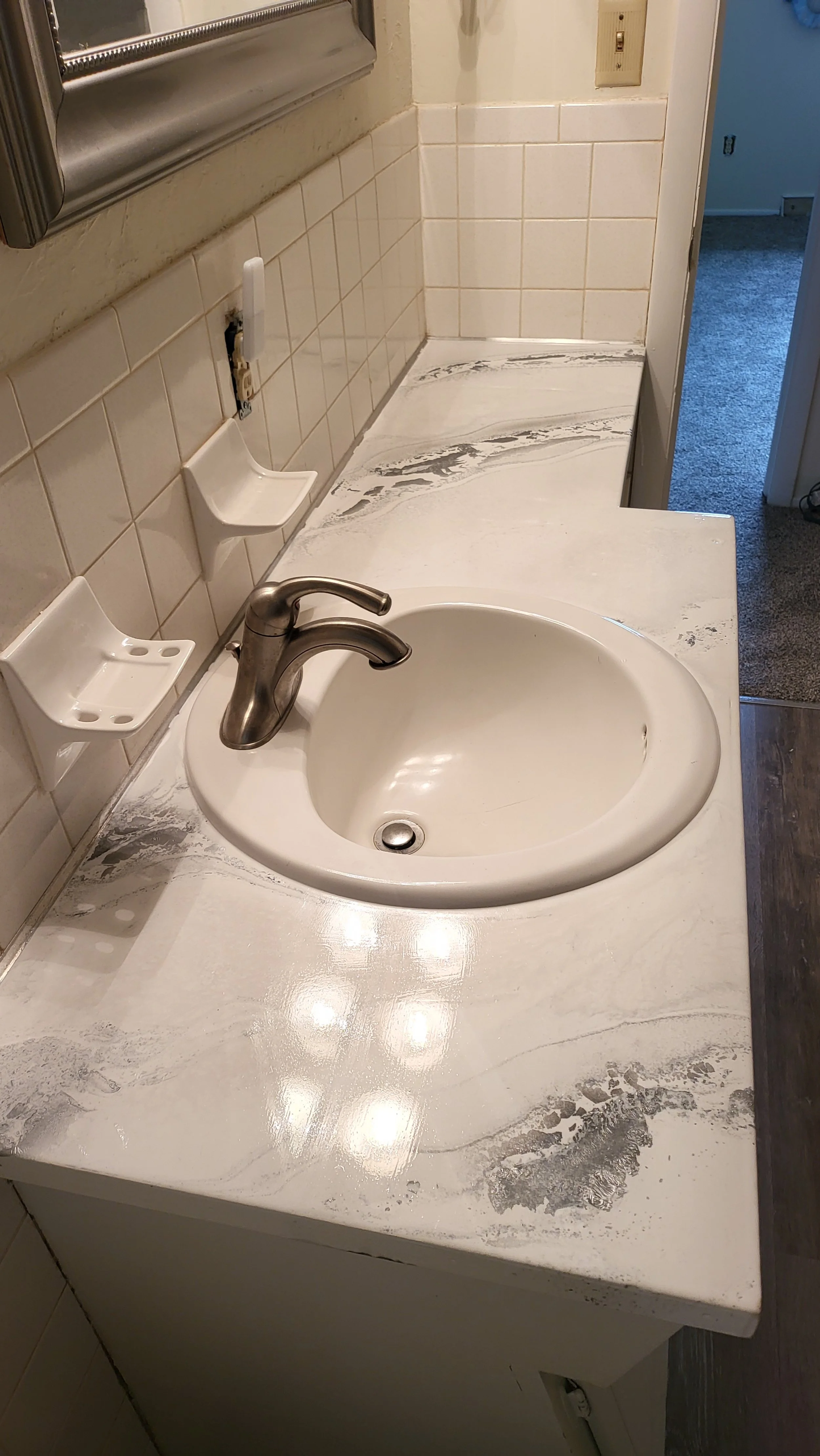 Bathroom epoxy countertop with a white sink, a silver faucet, beige tiles on the wall, and a mirror above.