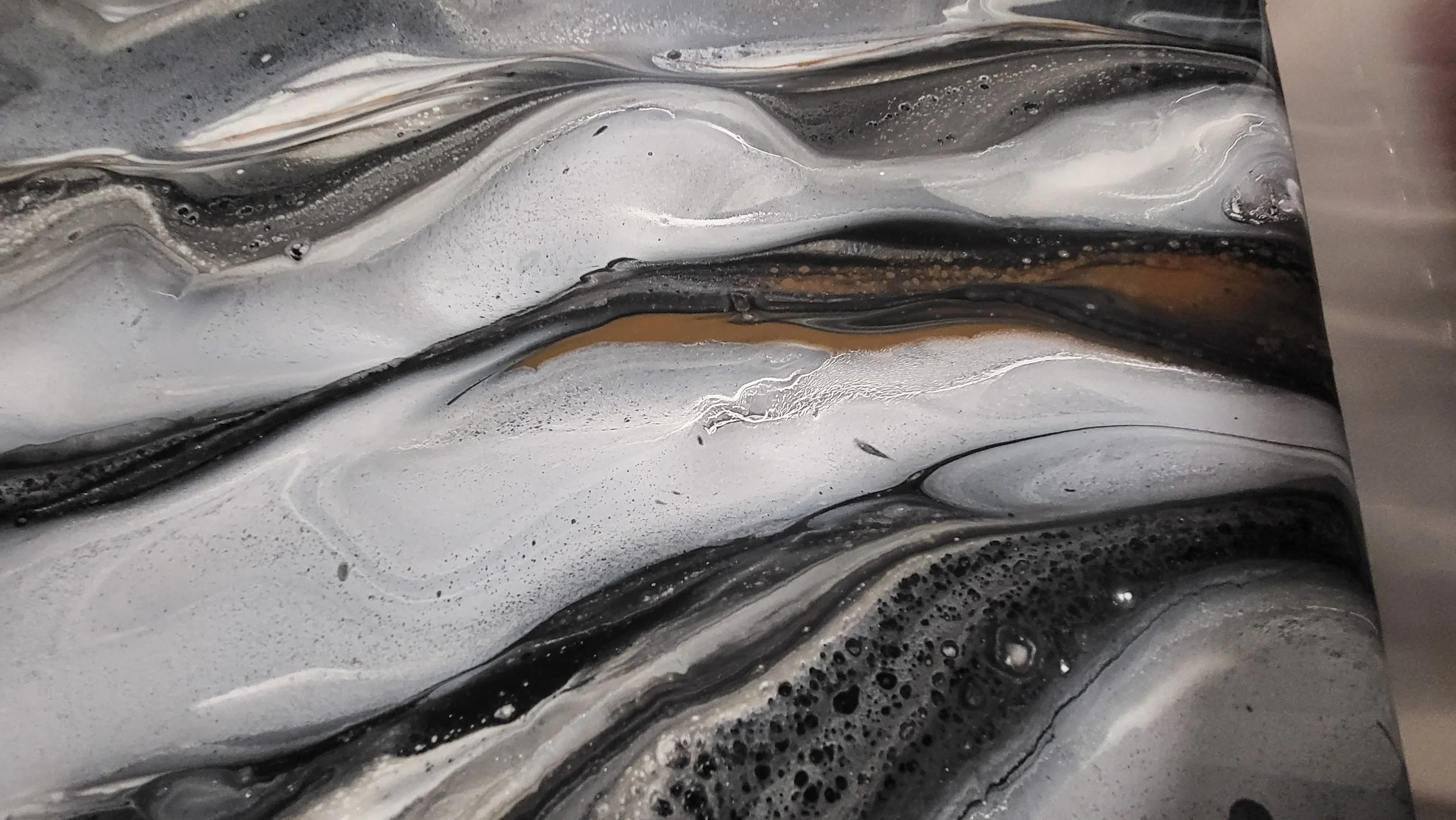 Close-up of black, white, and gray swirled marbled epoxy sample board surface with brown and gold accents.