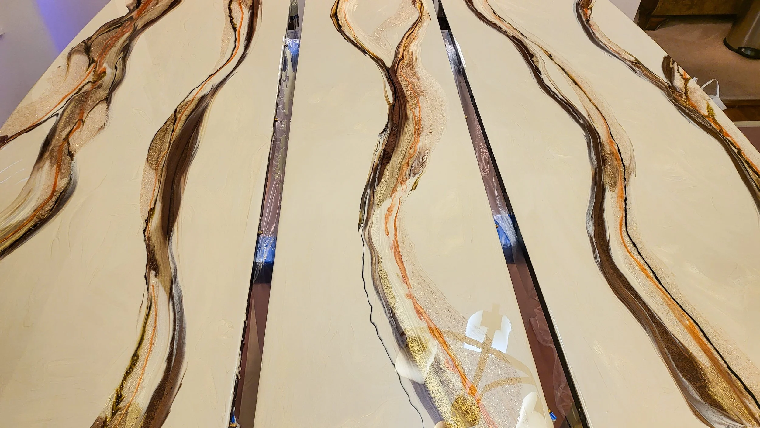 A close-up of a resin table with a cream background and flowing, wavy veins in shades of brown, black, tan, and orange.