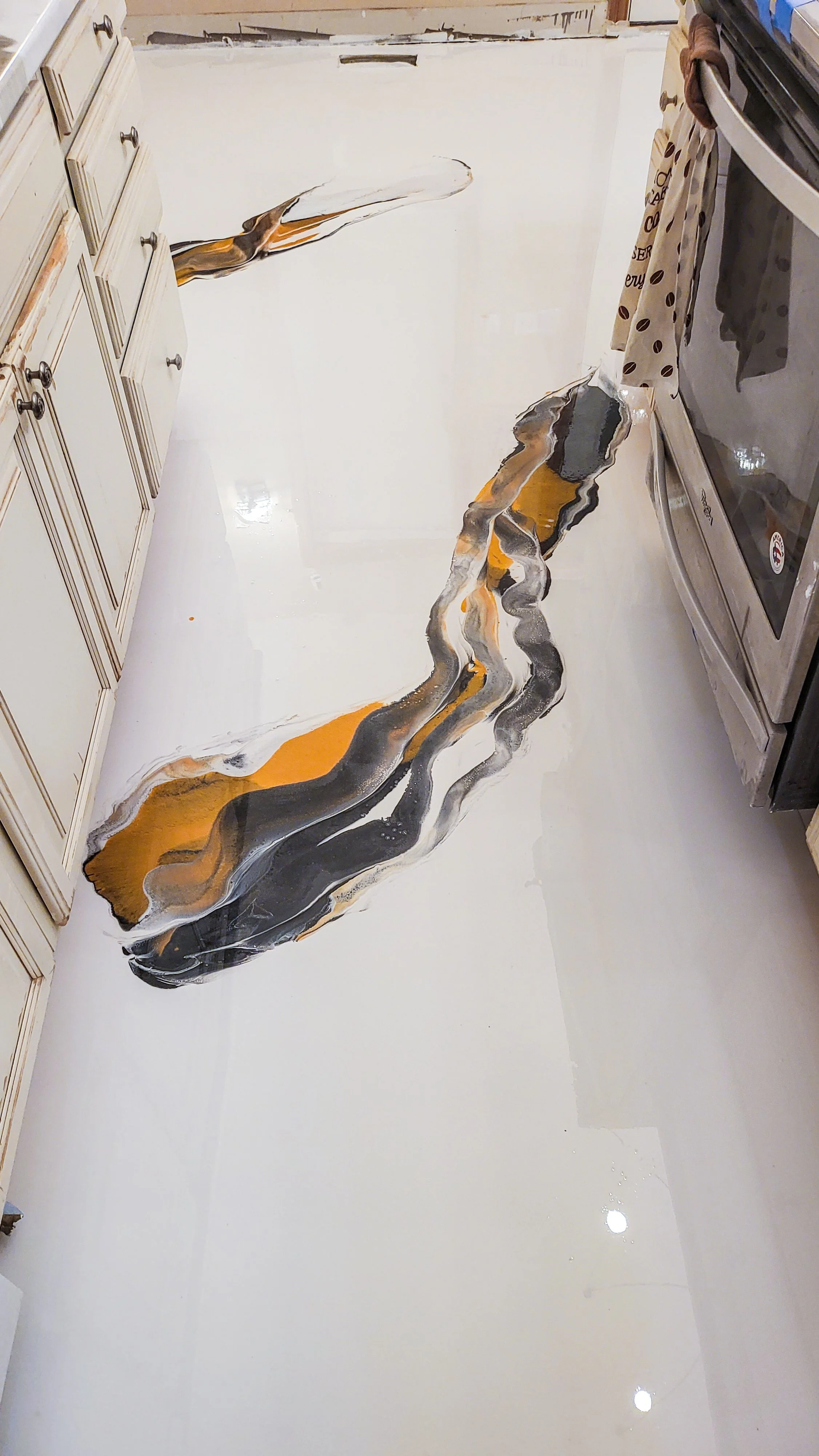 Kitchen epoxy floor with artificial river design painted in black, white, gray, and orange hues.