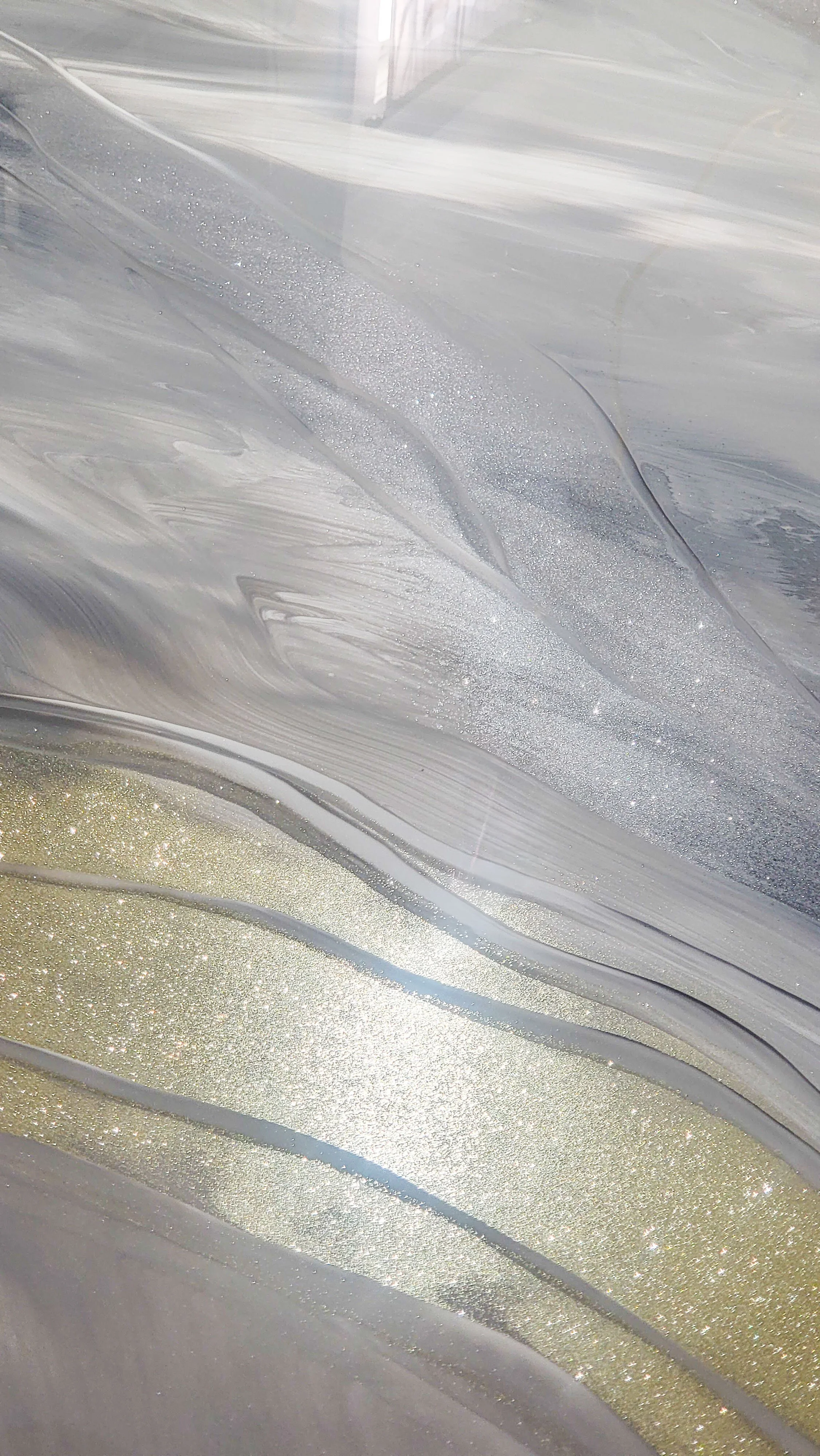 Close-up of a metallic epoxy surface with flowing patterns in silver, gray, and gold tones, accented with glittery and shimmery details.