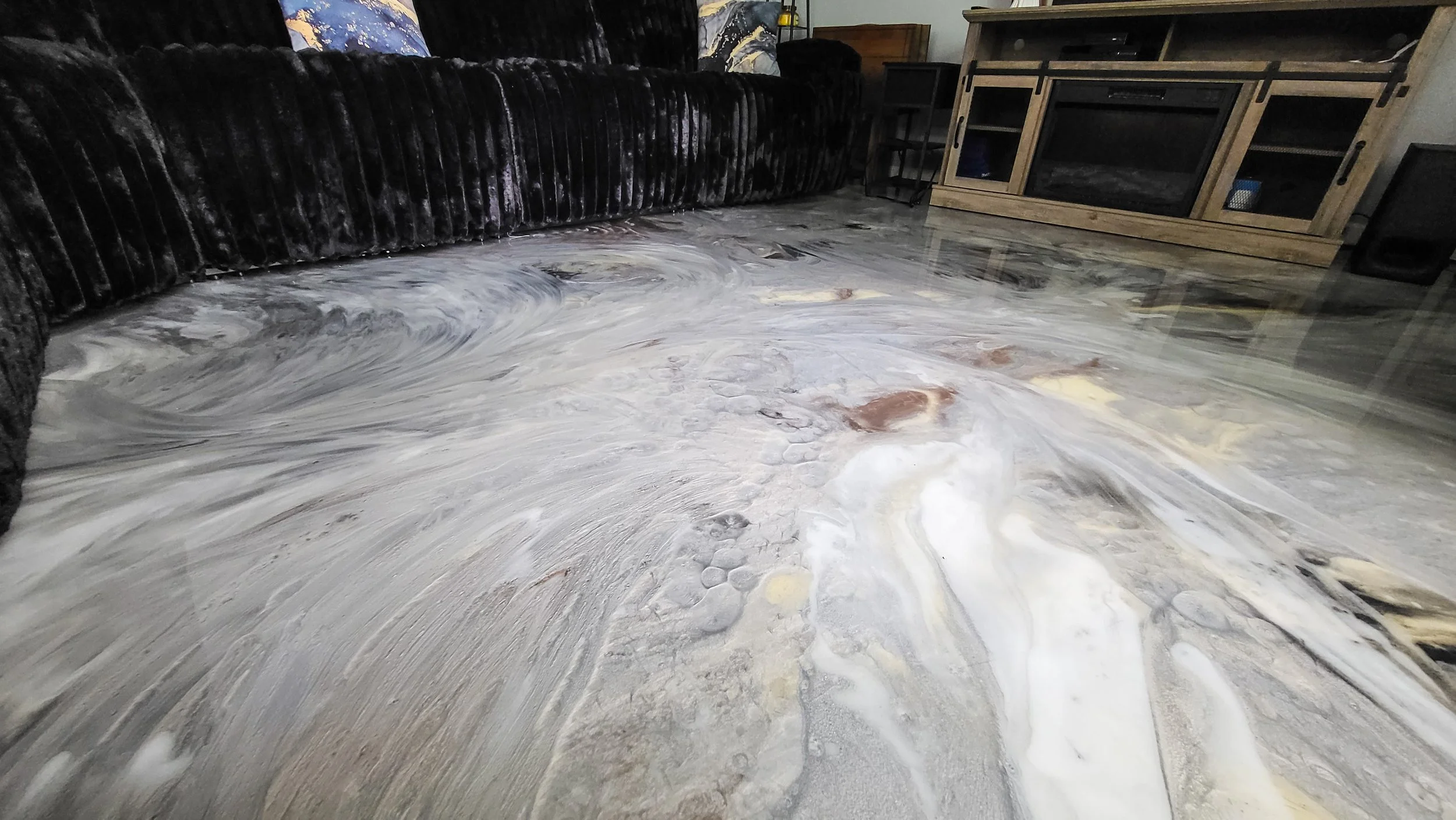Marbled epoxy flooring in living room with black sofa and wooden TV stand.