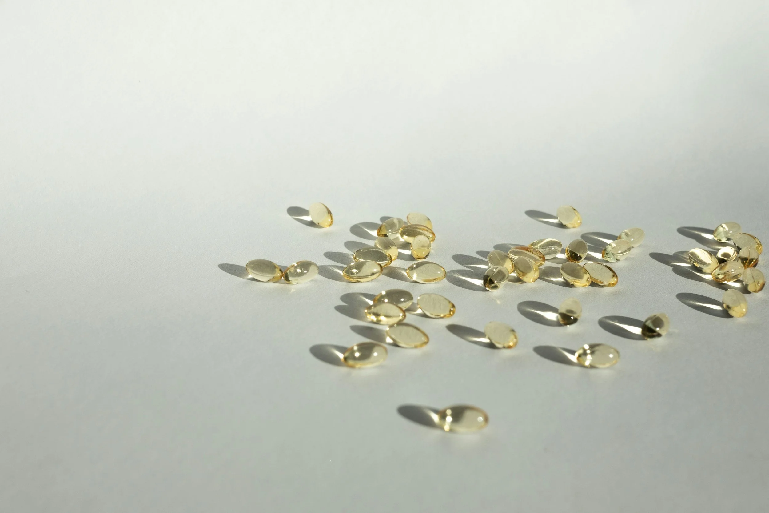Small, oval, translucent gel capsules scattered on a white surface with shadows.
