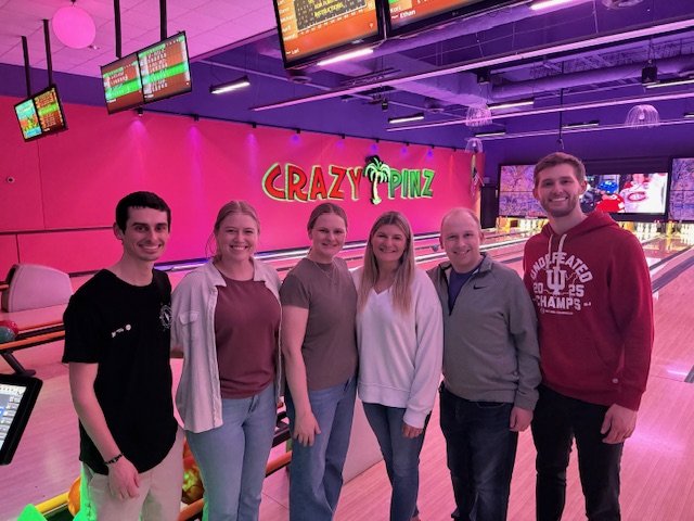 6 Occupational Therapists from Indiana Physical Therapy lined up for a photo while smiling and standing in a bowling alley at a business called Crazy Pinz