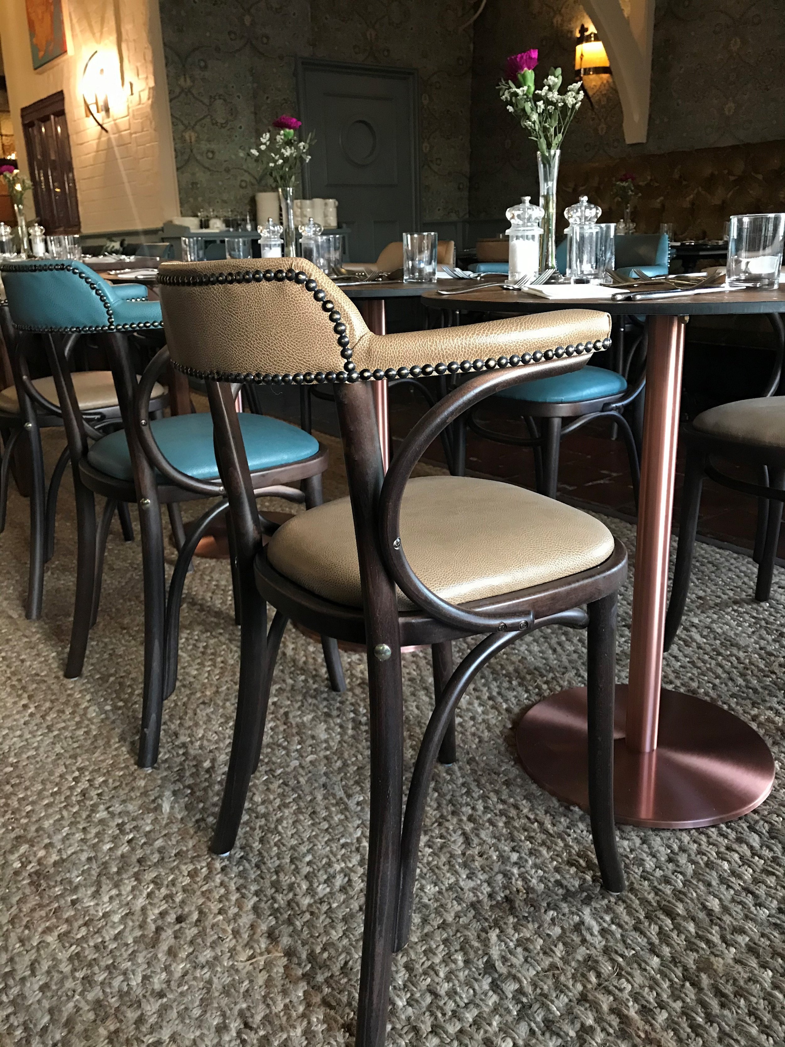 Dining table set with beige and teal chairs, topped with flowers, glassware, and silverware in a decorated restaurant.