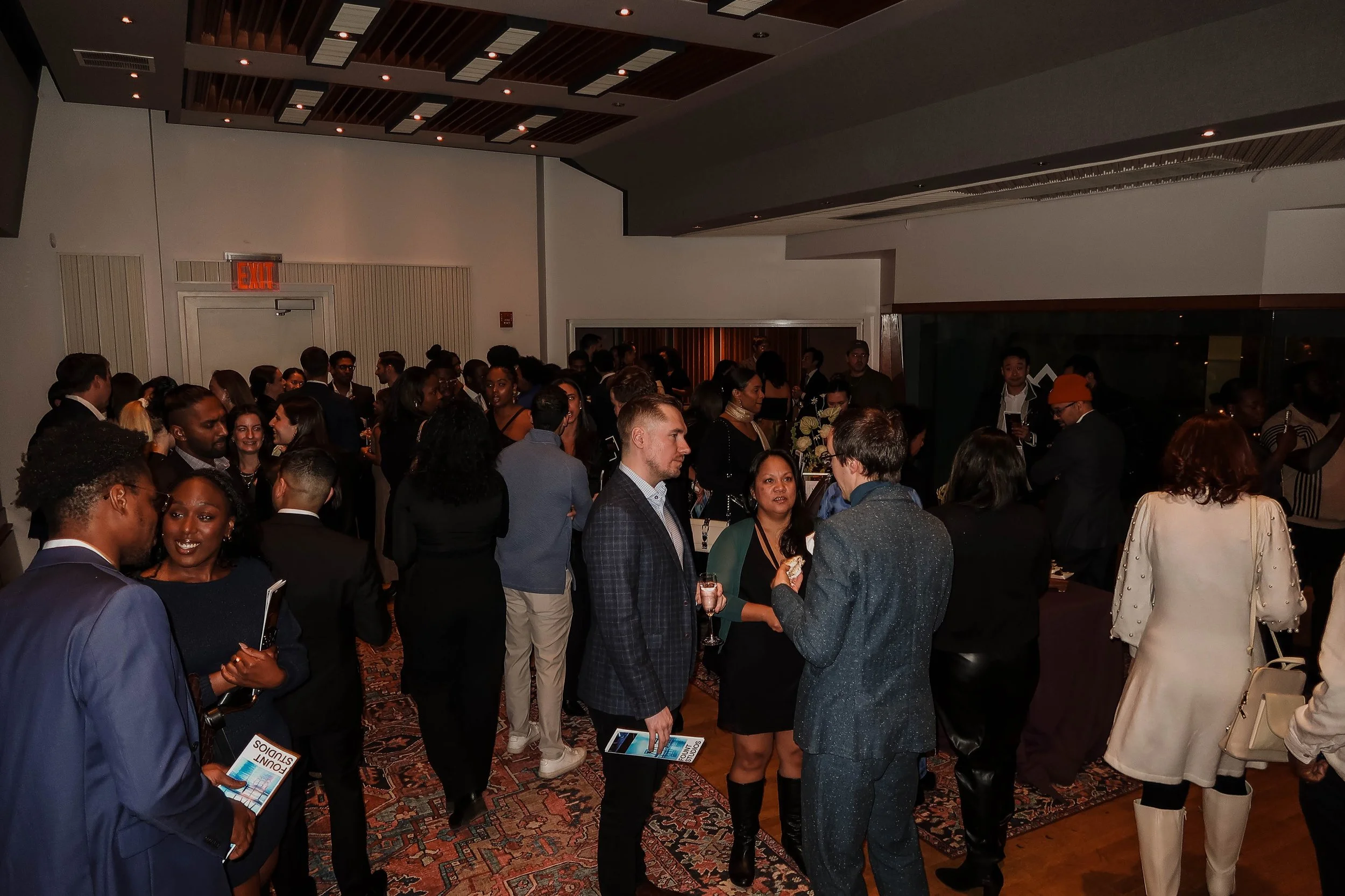 People socializing at a formal event in a well-lit indoor space, with some holding drinks and engaging in conversations.