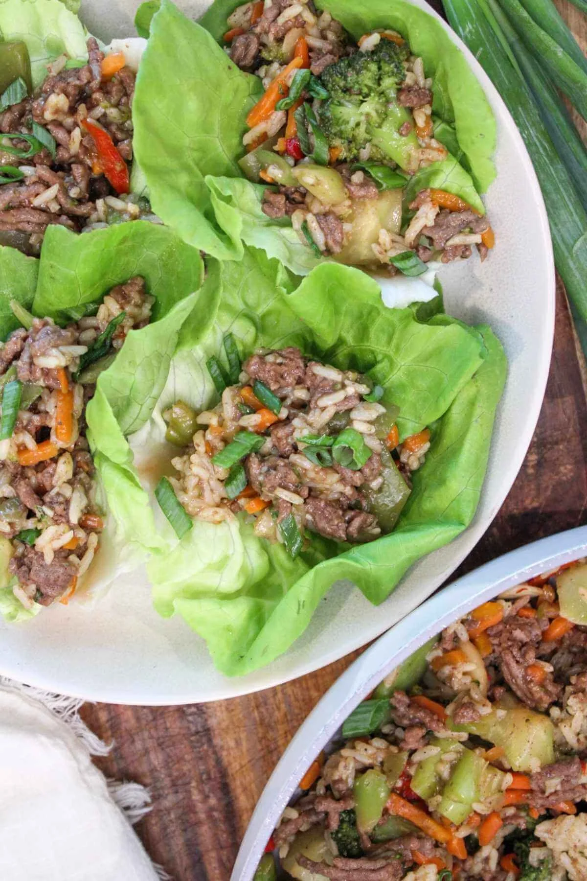 Plate of ground beef lettuce wraps topped with green onions and served on a wooden platter.
