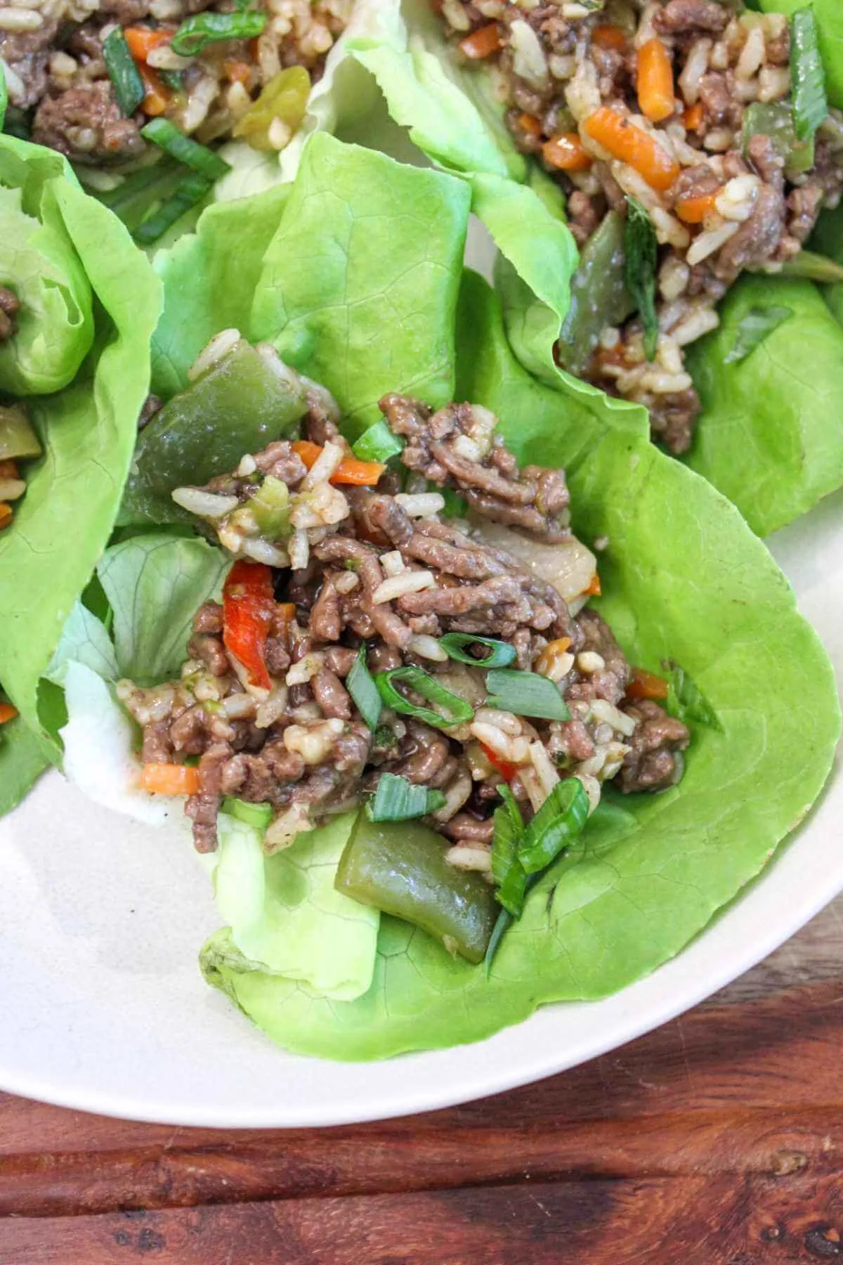 Ground beef lettuce wraps on a white plate. The lettuce wraps are full of a ground beef and jasmine rice mixture thats filled with stir fry vegetables and topped with green onions.