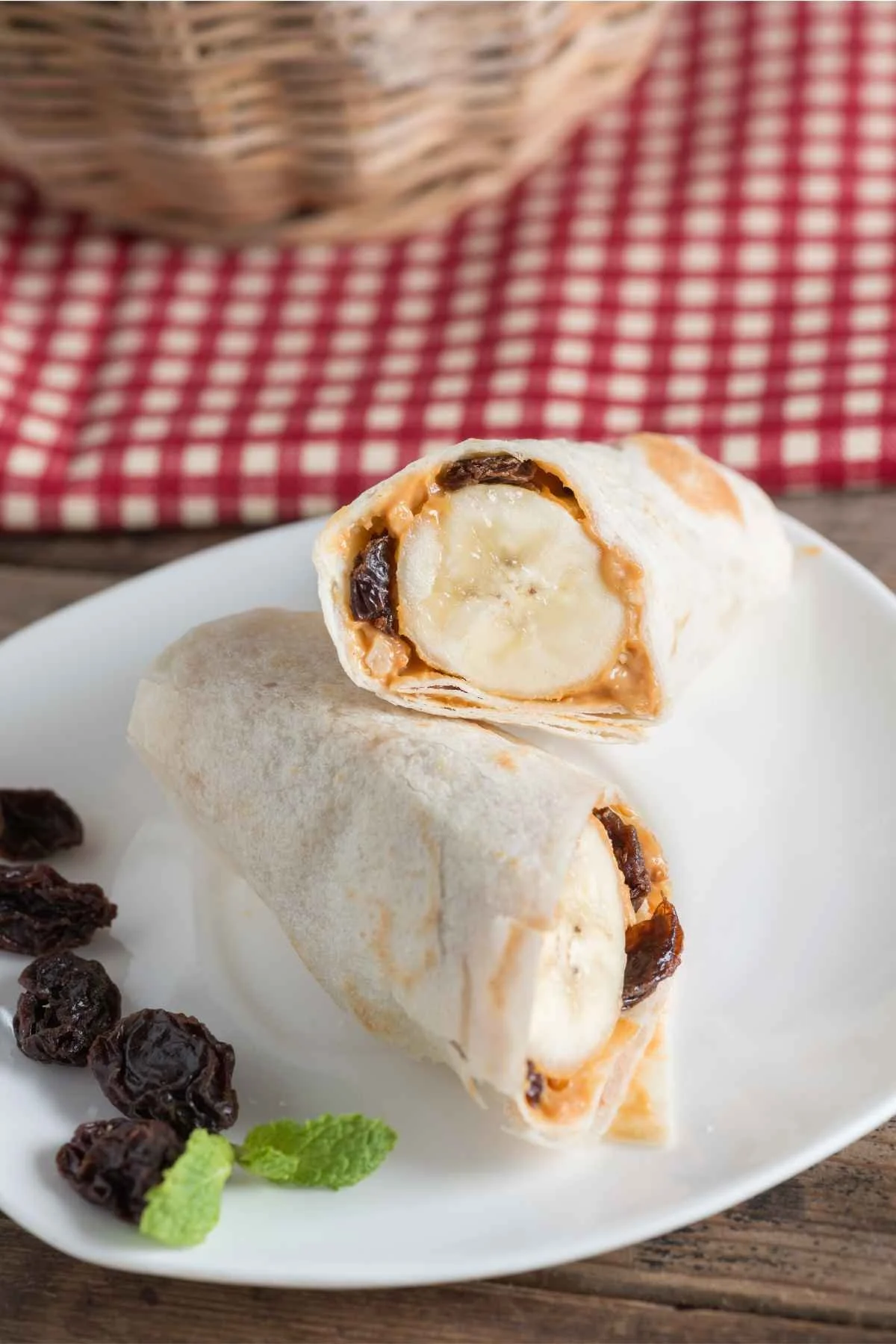 Tortilla full of peanut butter, banana, and raisins then rolled up into a tube and served on a white plate.