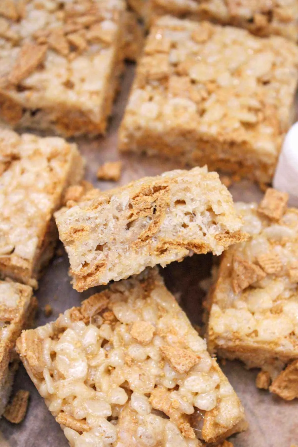 brown butter golden graham Rice Krispie treats served on parchment paper with one flipped sideways to see the texture. The Rice Krispies look light, fluffy, and delicious!