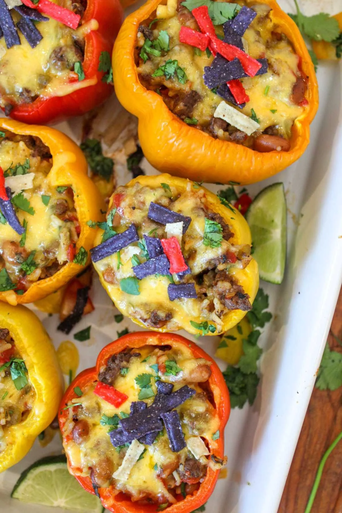 Colorful stuffed bell peppers filled with cheese, ground meat, and herbs, garnished with red and blue tortilla strips, set on a white tray.